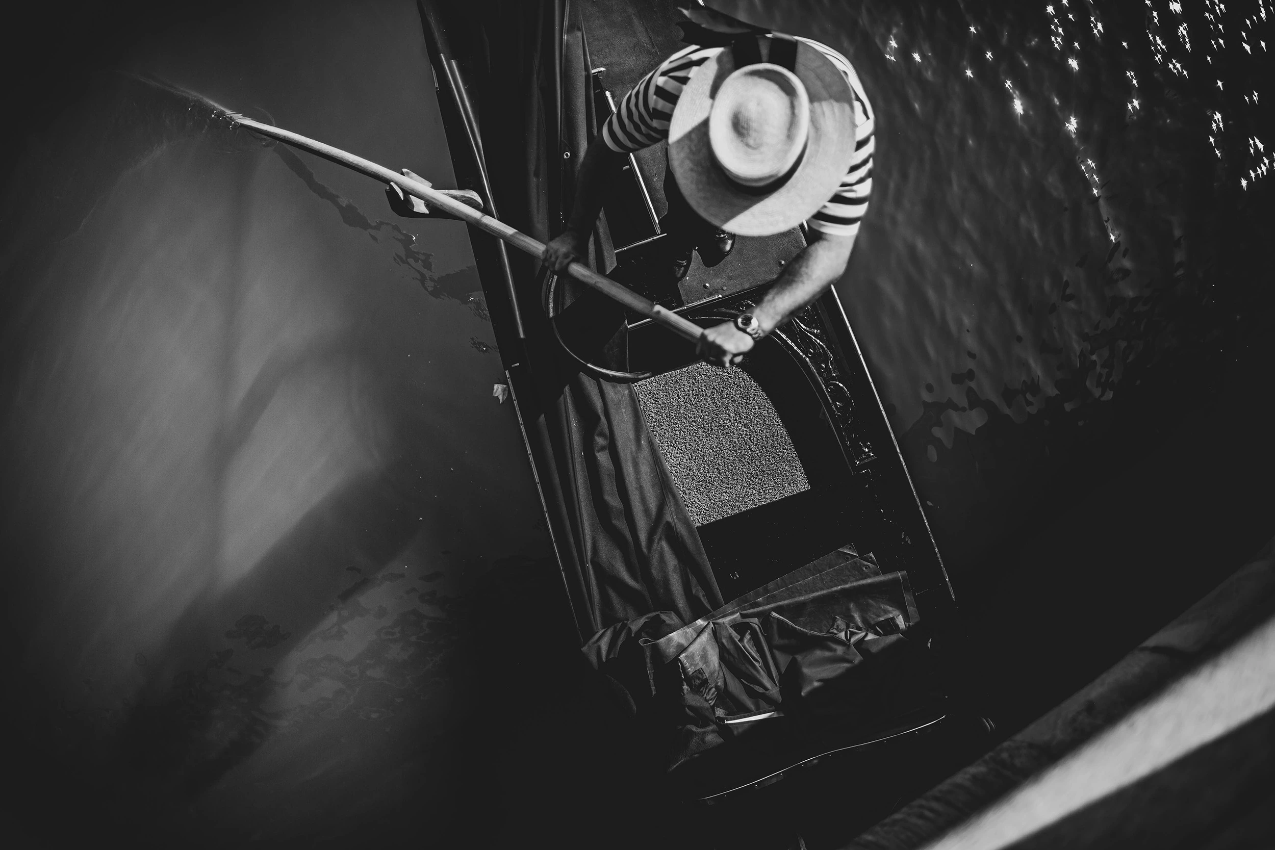 From inside a gondola, the gondolier's straw hat and oar backlit over the water.