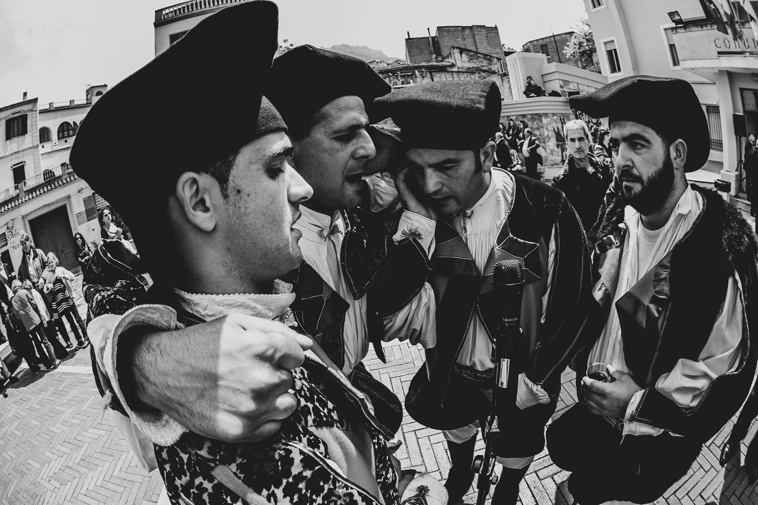 Four men in Sardinian costume, wearing the black berritta, waiting along the street.
