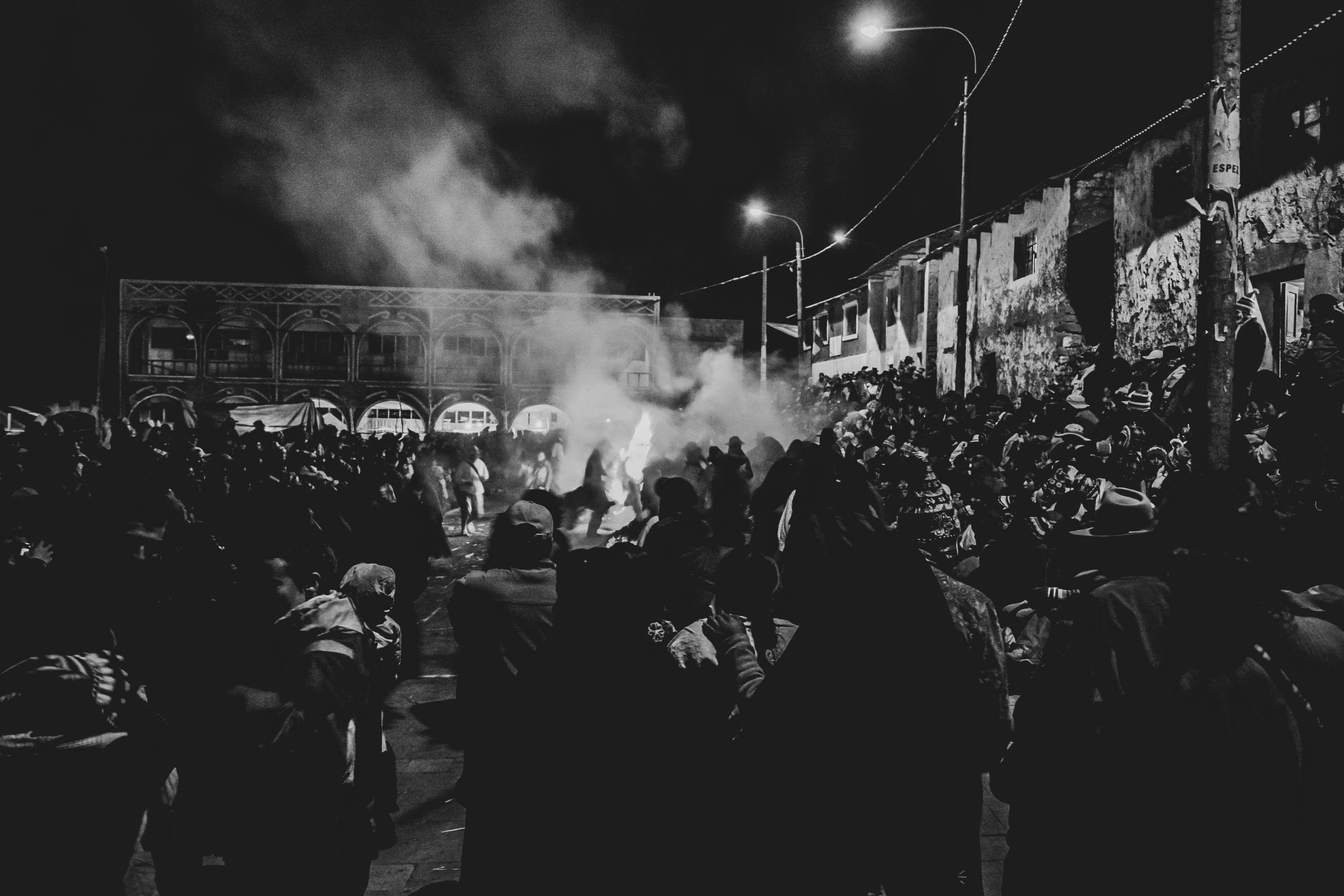 At night, the crowd fills the village street around a smoking fire.