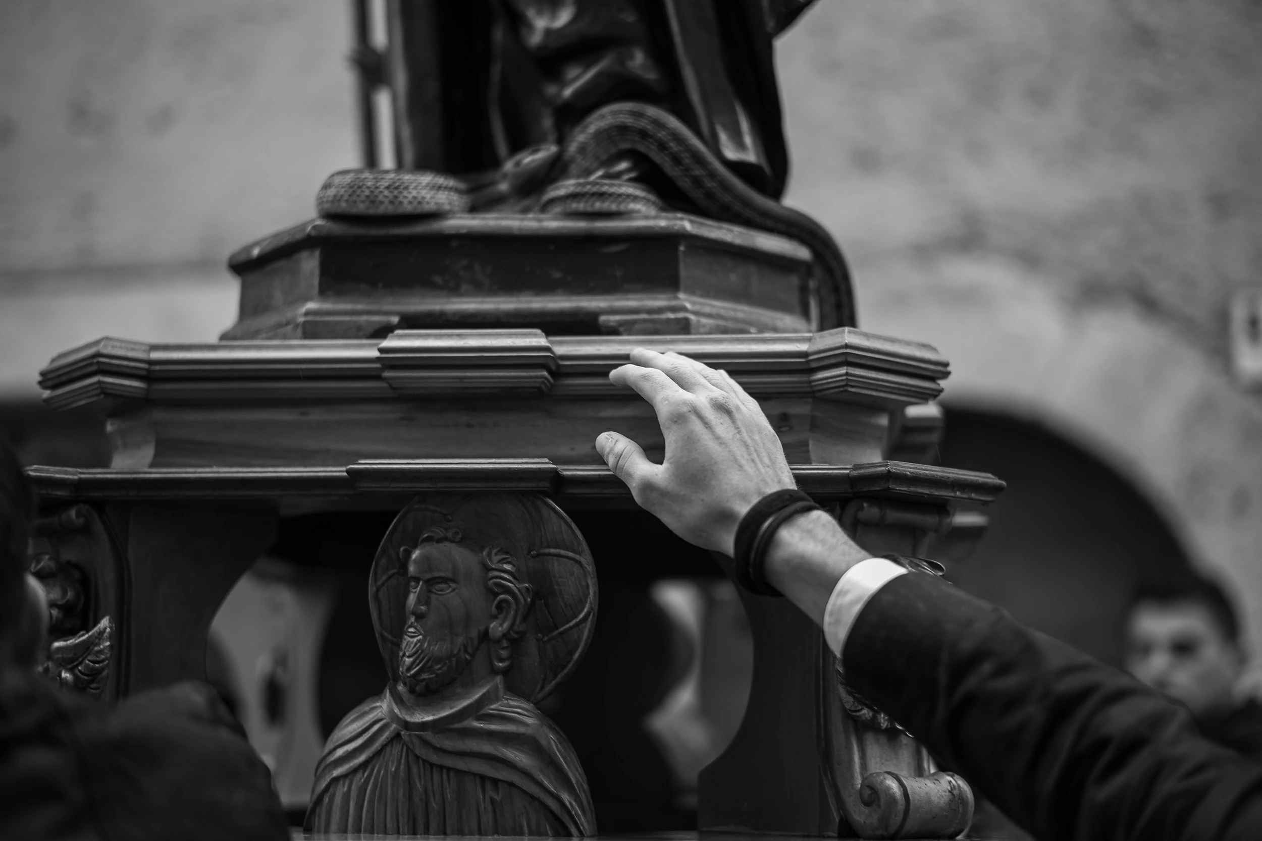 A hand resting on the carved base of a processional statue, with the bas-relief of a saint.
