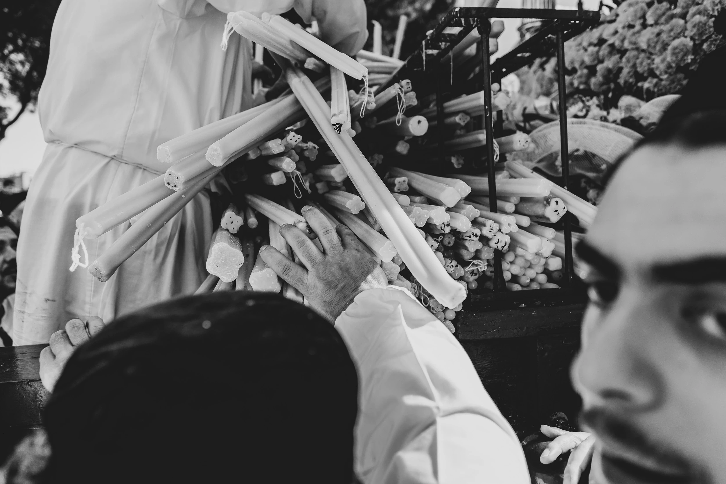 The hands of a devotee in a white robe grip bundles of candles.