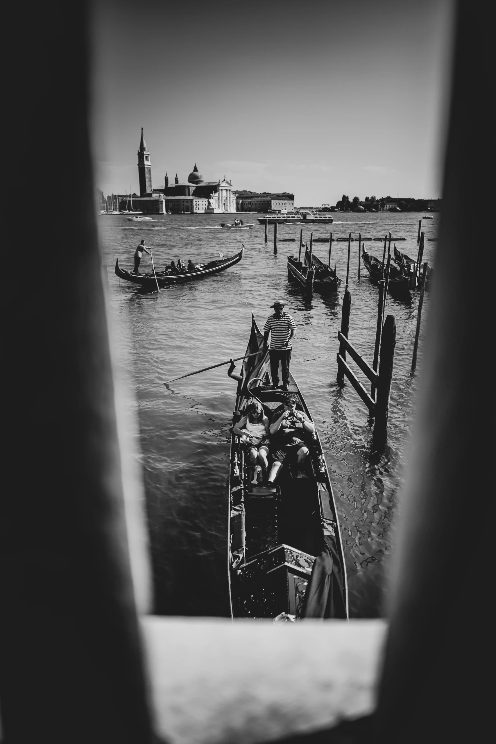 Through a narrow gap, the basin with the campanile of San Giorgio Maggiore and gondolas moored to poles.