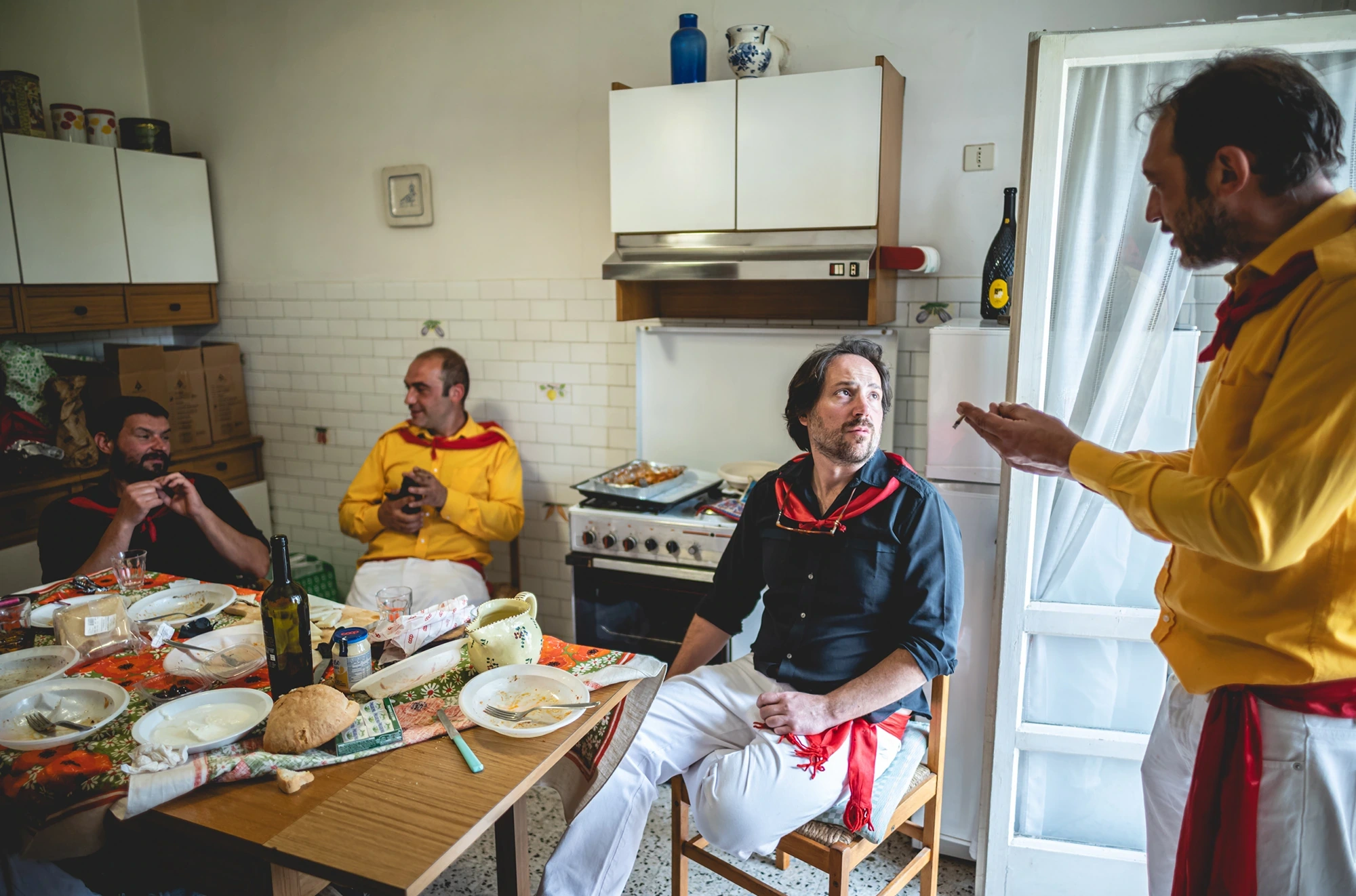 In a kitchen, the ceraioli in yellow shirts around the table.