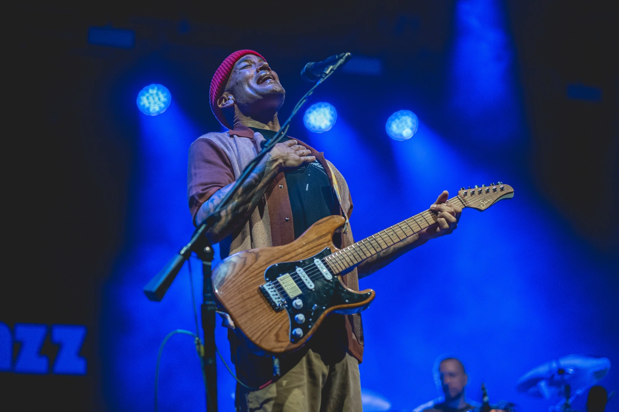 In blue light, head thrown back at the microphone, guitar in hand.