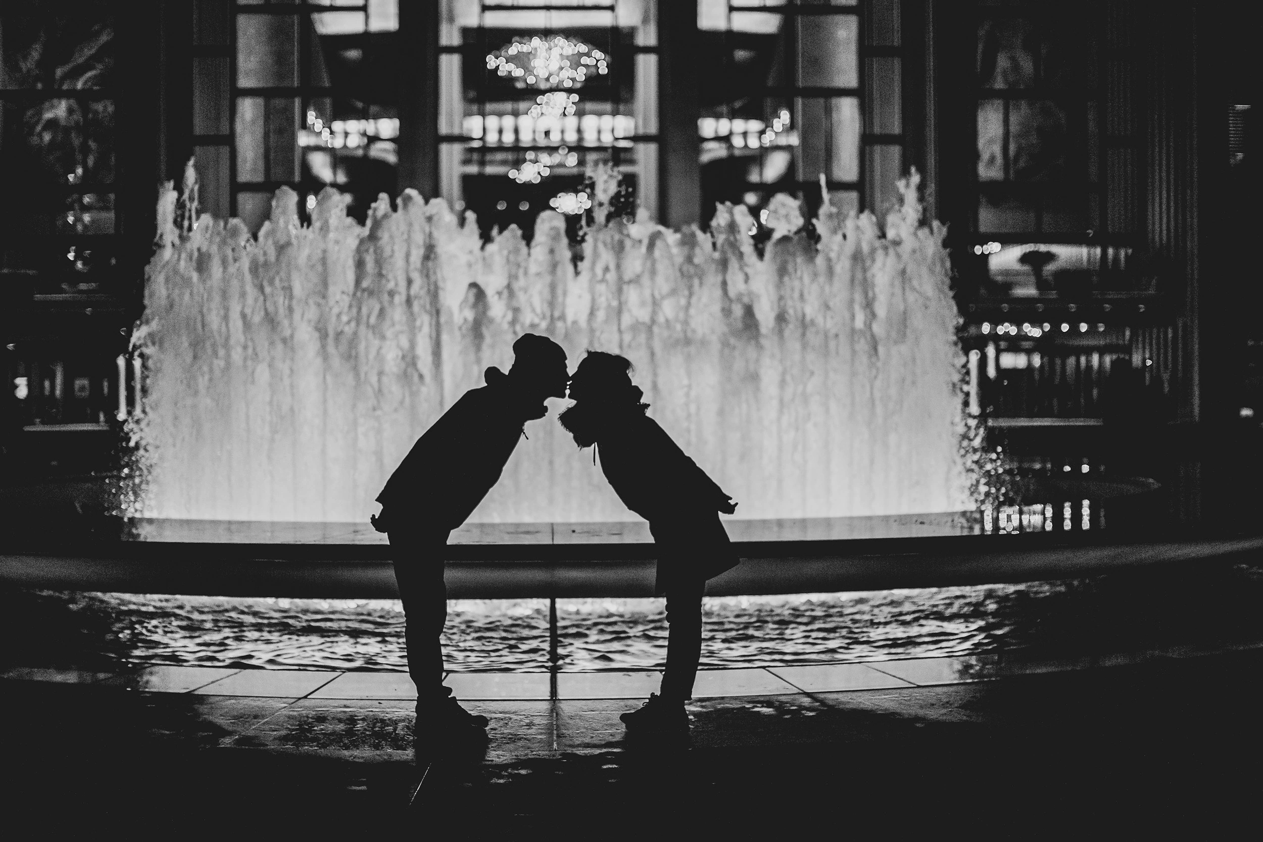 Two children in silhouette, face to face on the rim of a fountain.