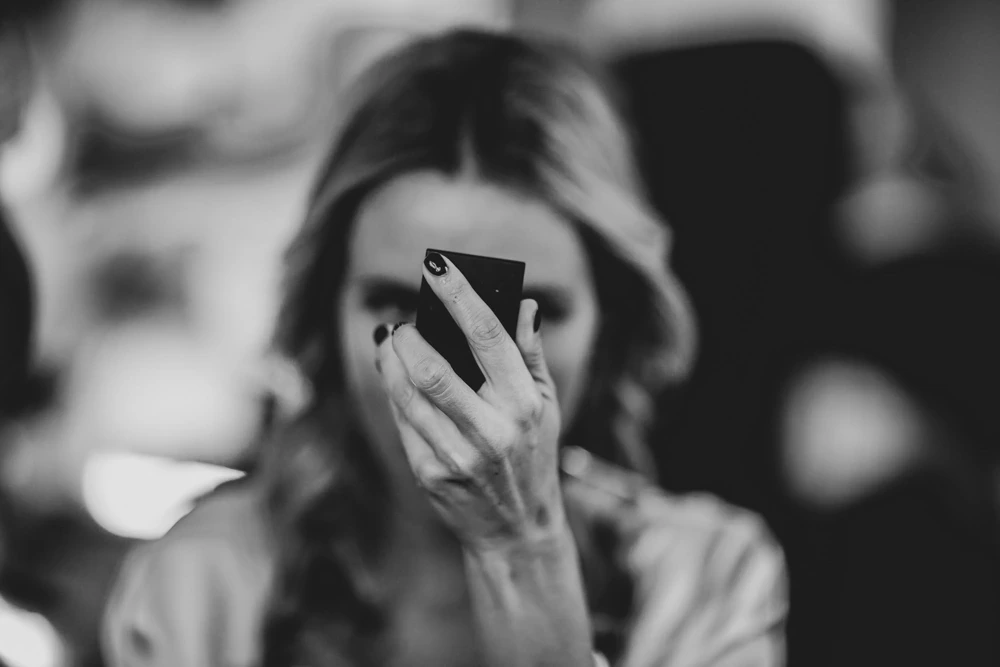 Make-up at a hand mirror, among out-of-focus reflections.