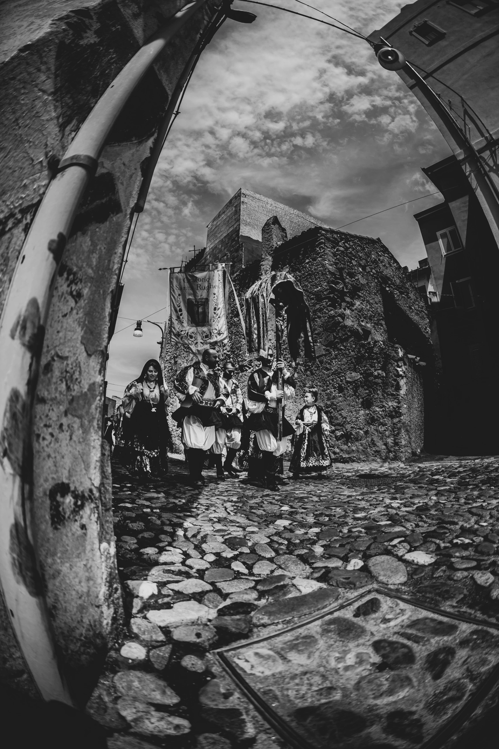 Through an archway, the costumed procession climbs the stone street.