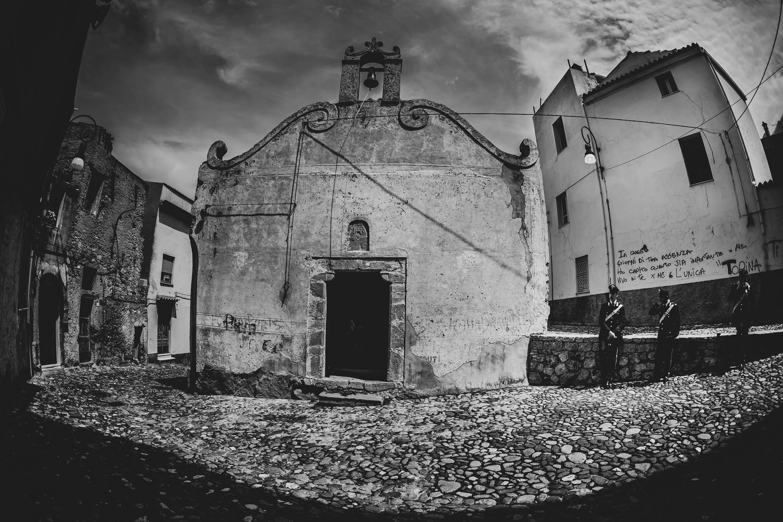 The village chapel with its scrolled gable, on the empty cobblestones.