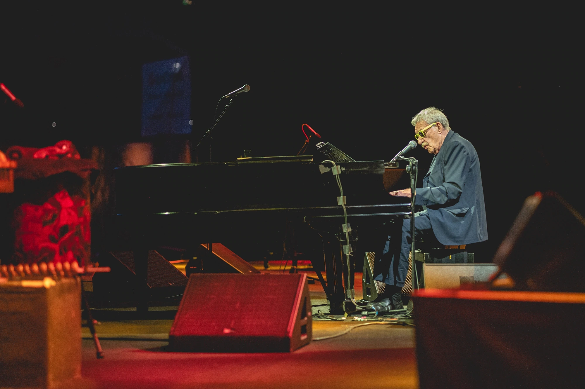 A pianist at the grand piano, among monitors lit in red.