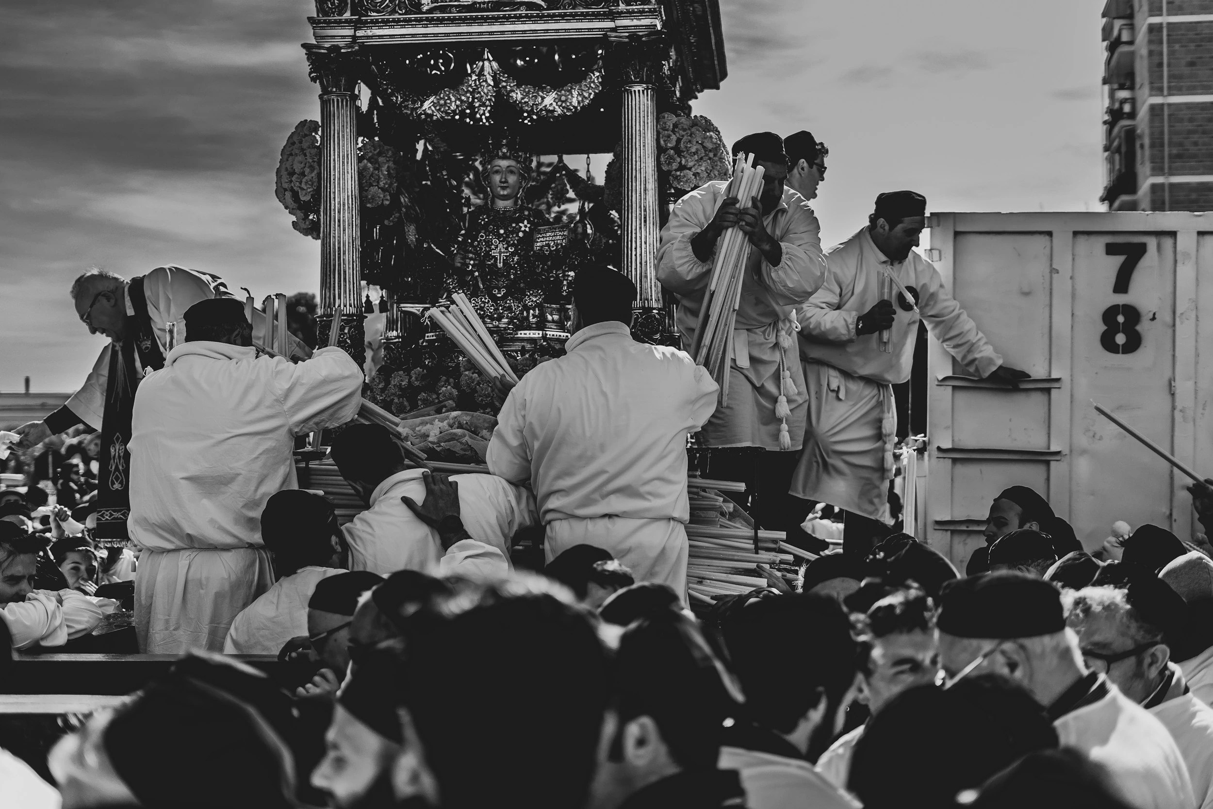 Devotees in white around the fercolo, pressed against a container in the middle of the street.