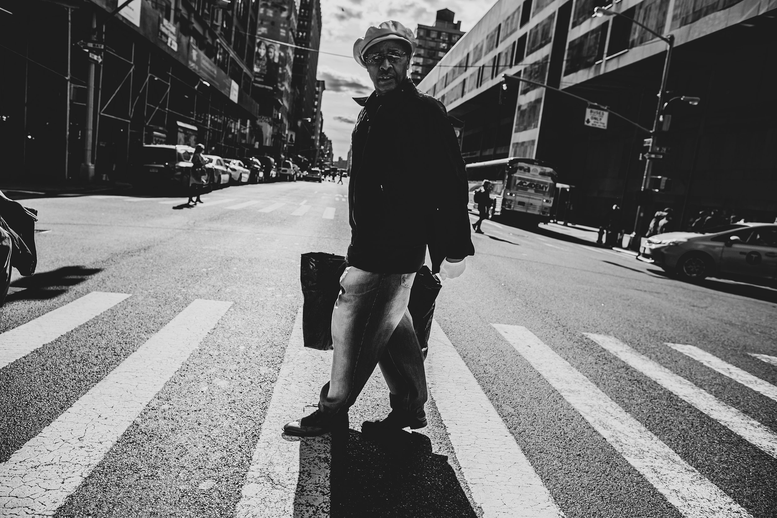 A man in a hat stops in the middle of the crossing, a bag in his hand.