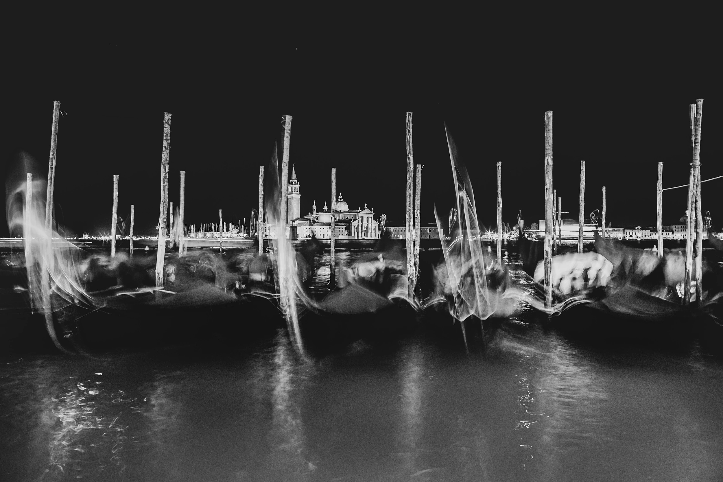 A long exposure at dusk: gondolas stirred by the water among the mooring poles.