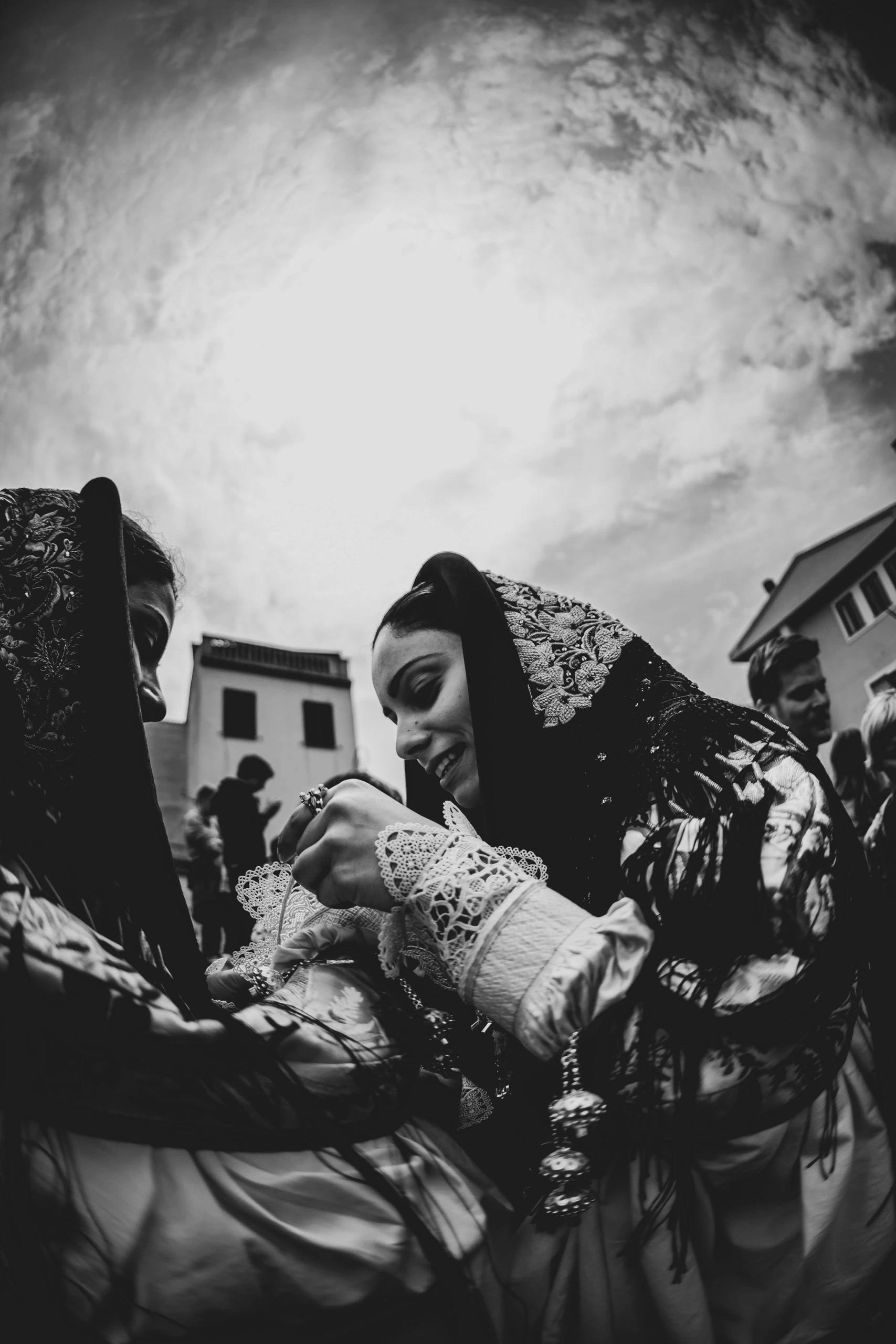 Two women in costume: one adjusts the other's dress under a heavy sky.