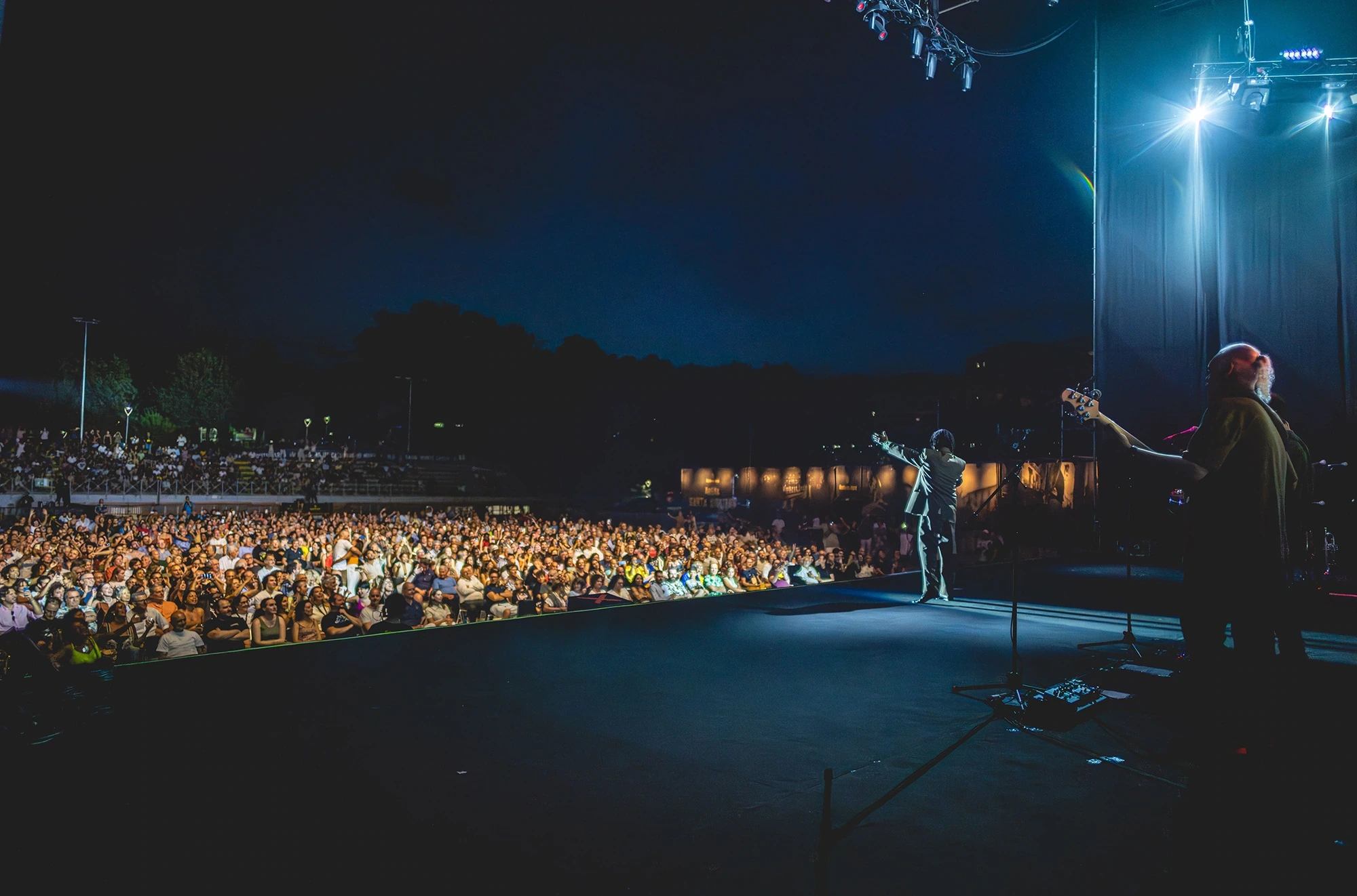 From the stage, the audience of an open-air concert spread out in the dark.