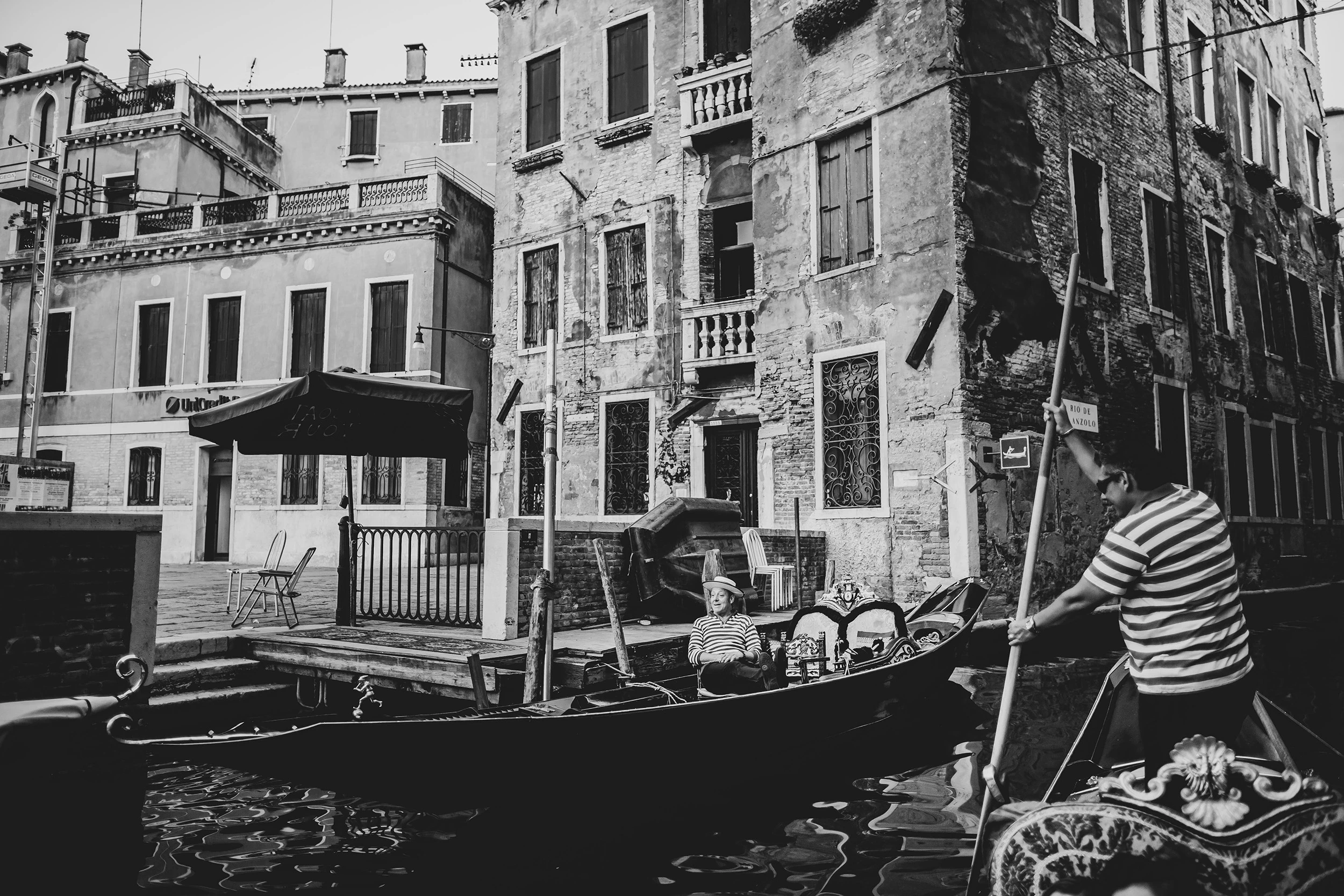 A gondolier pushes on his oar in a square facing the canal, among the moored gondolas.