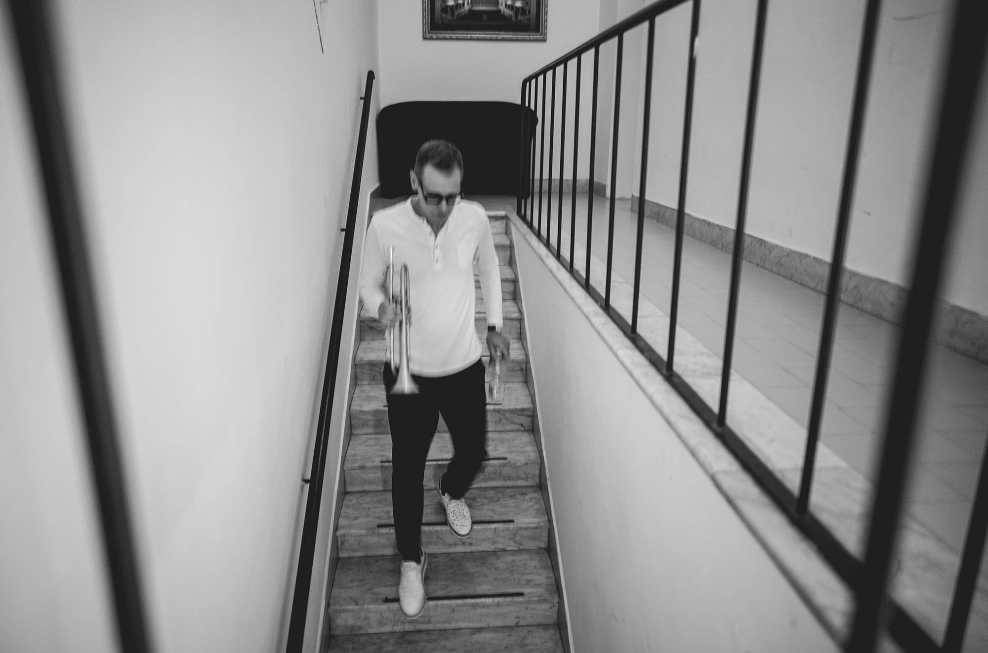In black and white, a figure comes down the stairs backstage.