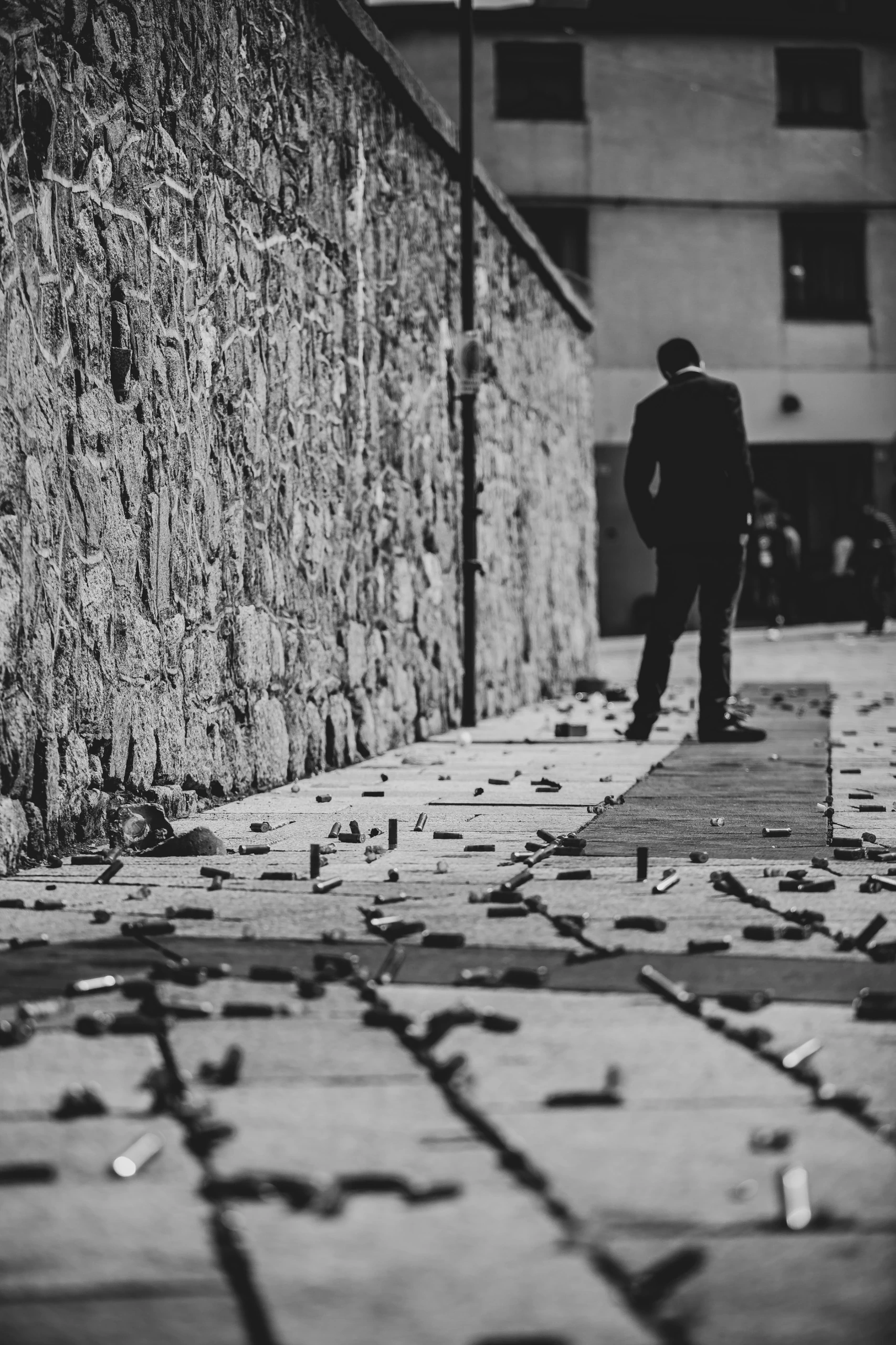 A man walks away along the stone wall, among the spent fireworks scattered on the ground.