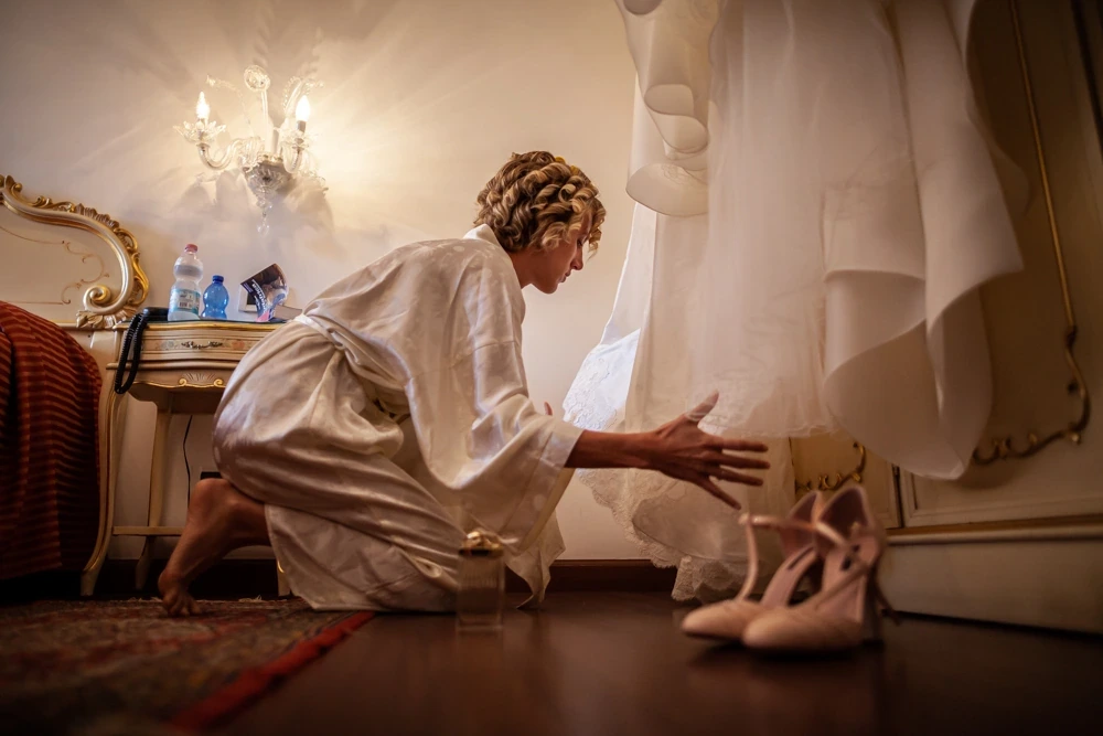 Crouched beneath the hanging dress, arranging the shoes on the parquet.