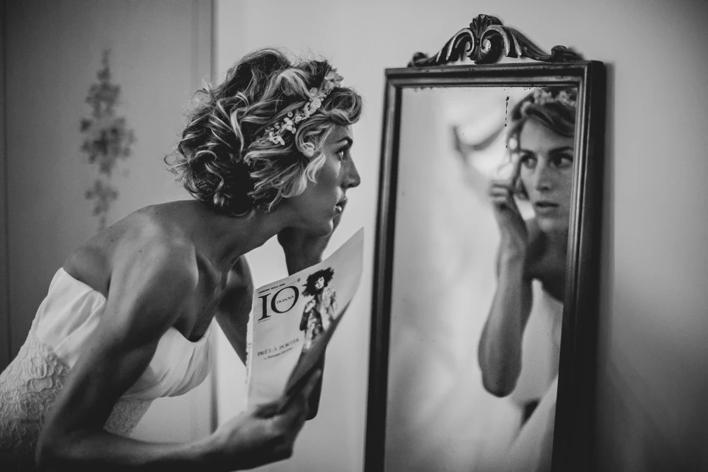 In front of the mirror, leafing through a magazine beside her own reflection.