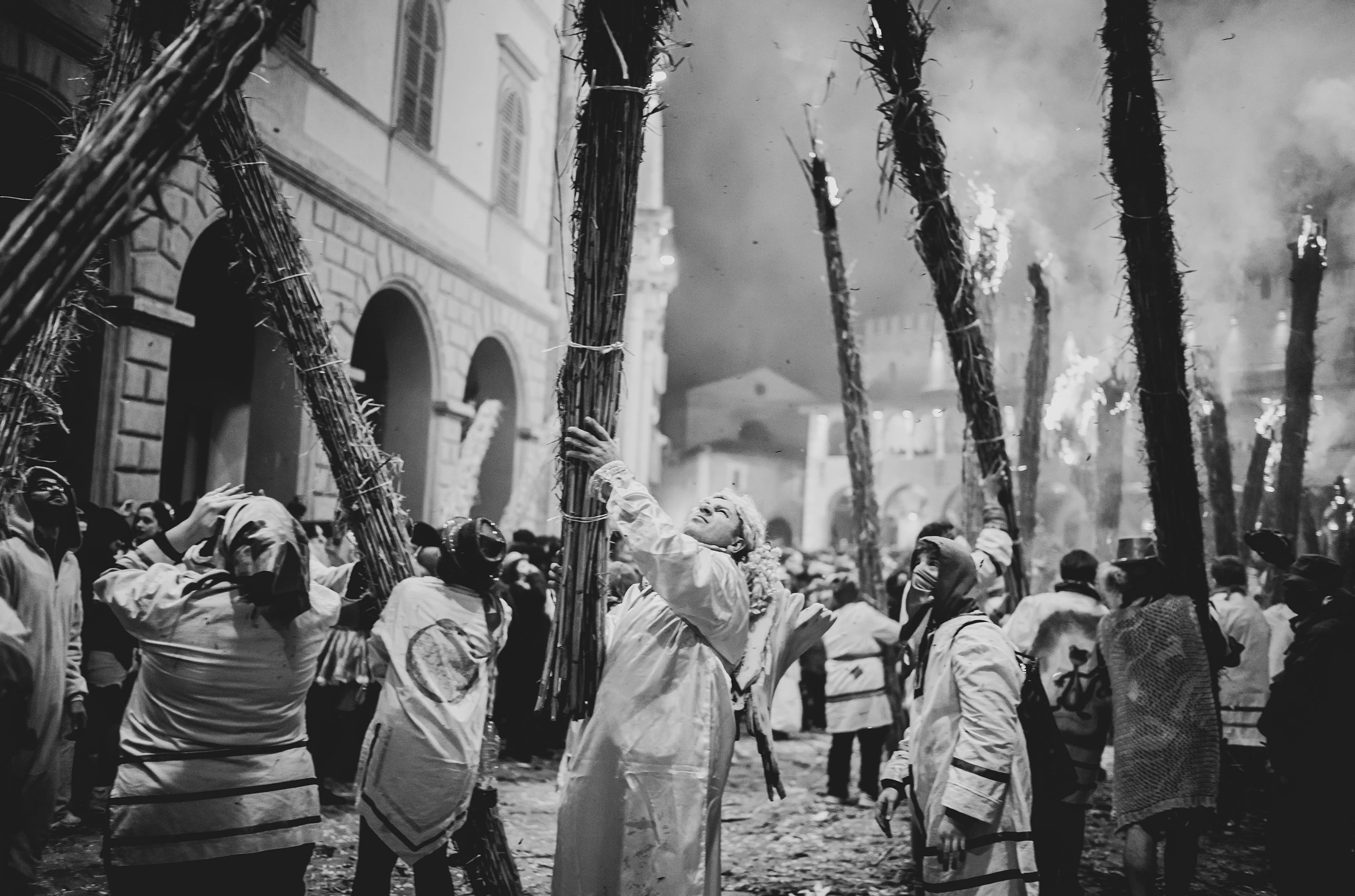 A crowd in white costume with the burning bundles raised above their heads.