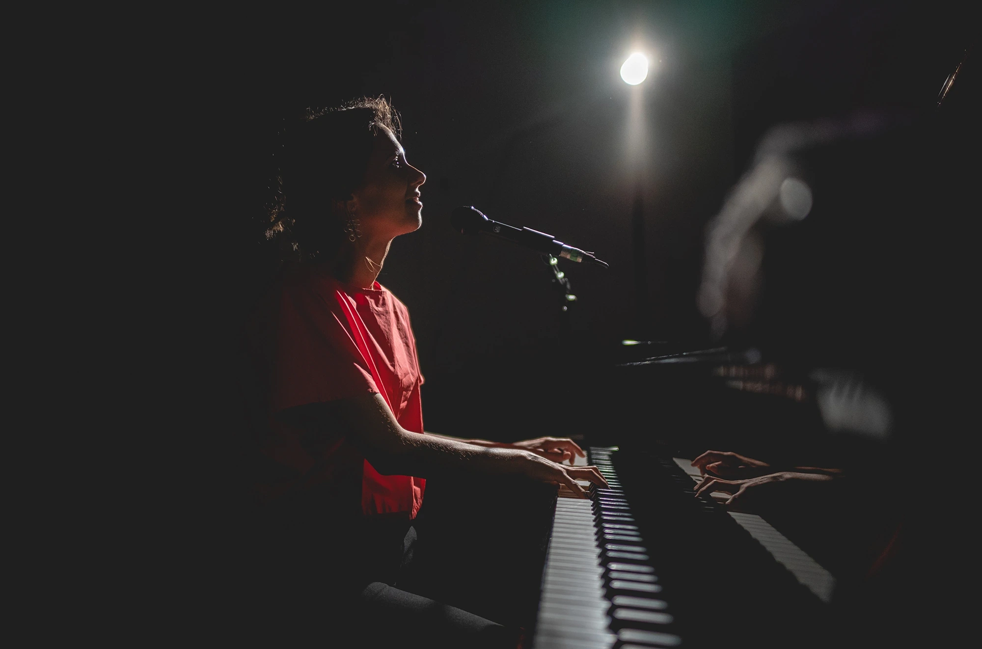 Under a single beam of light, singing at the keyboard.