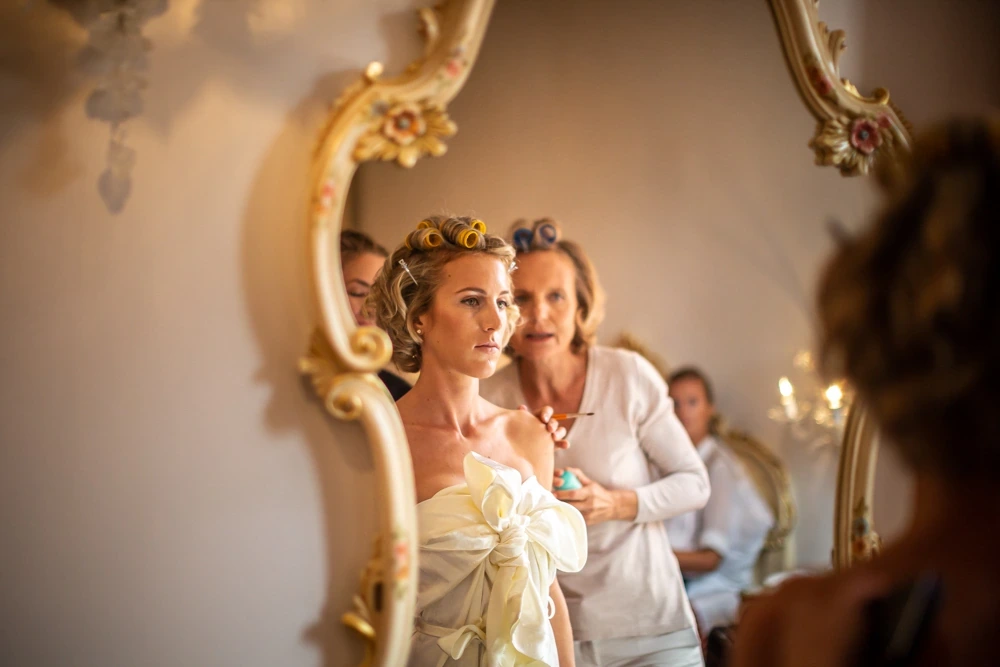 In the gilded mirror, the bride and two women around her.