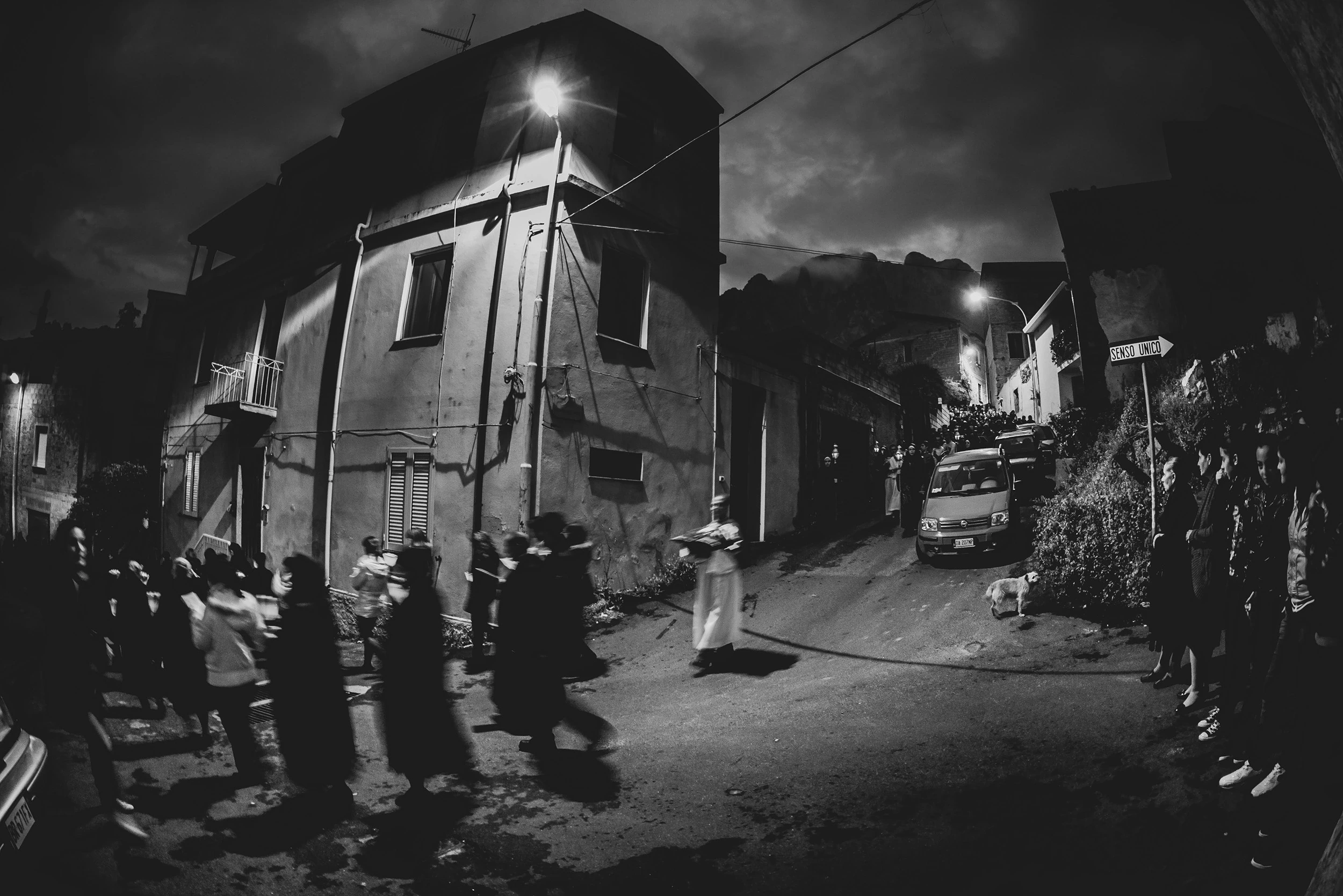 At night, the costumed figures along the village street beneath the streetlamps.