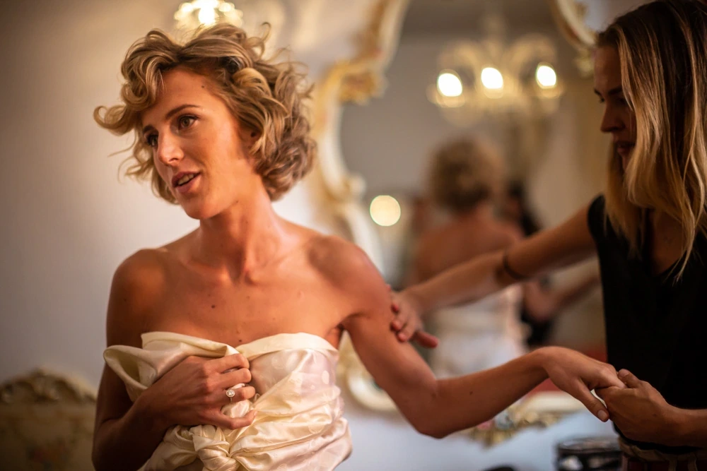 The bride holds up her dress while it is fastened.