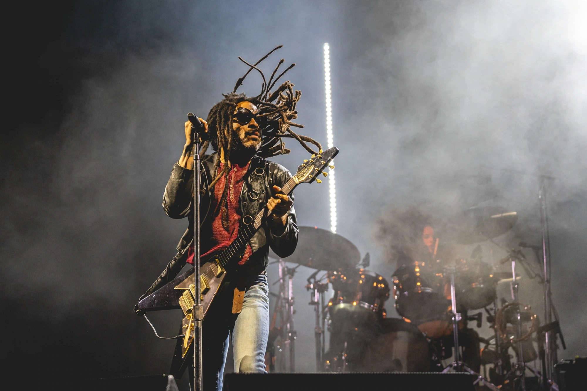 Through the smoke, a musician with an elaborate headdress in front of the drums.