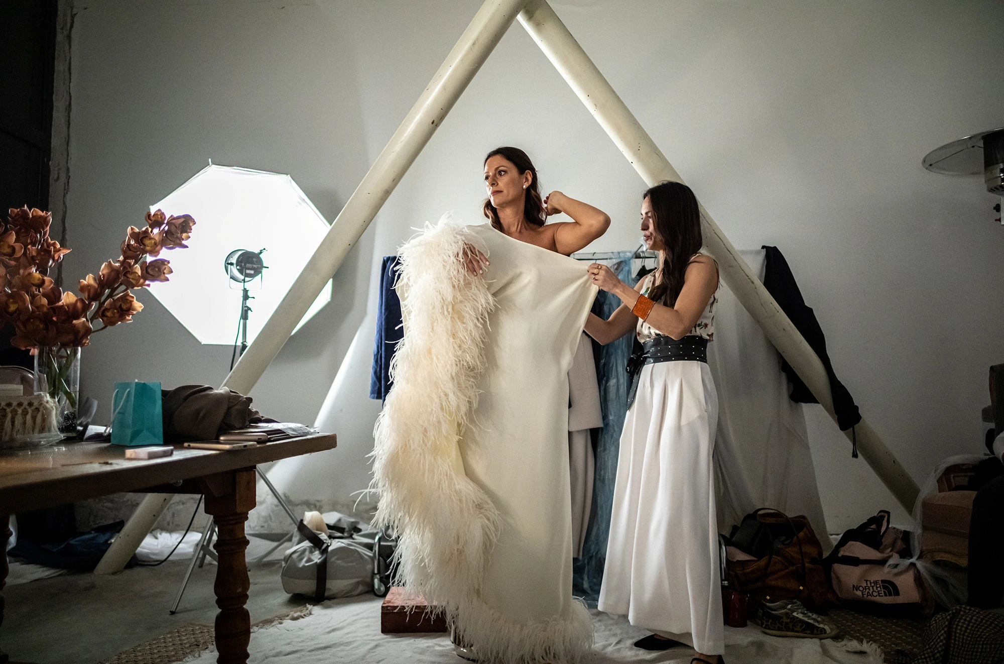In a room set up with a softbox, the bride waits as a feather stole is handed to her.