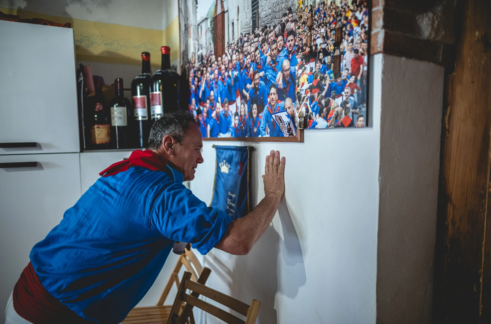 A ceraiolo in a blue shirt leaning on the wall, beside a large photograph of the feast.