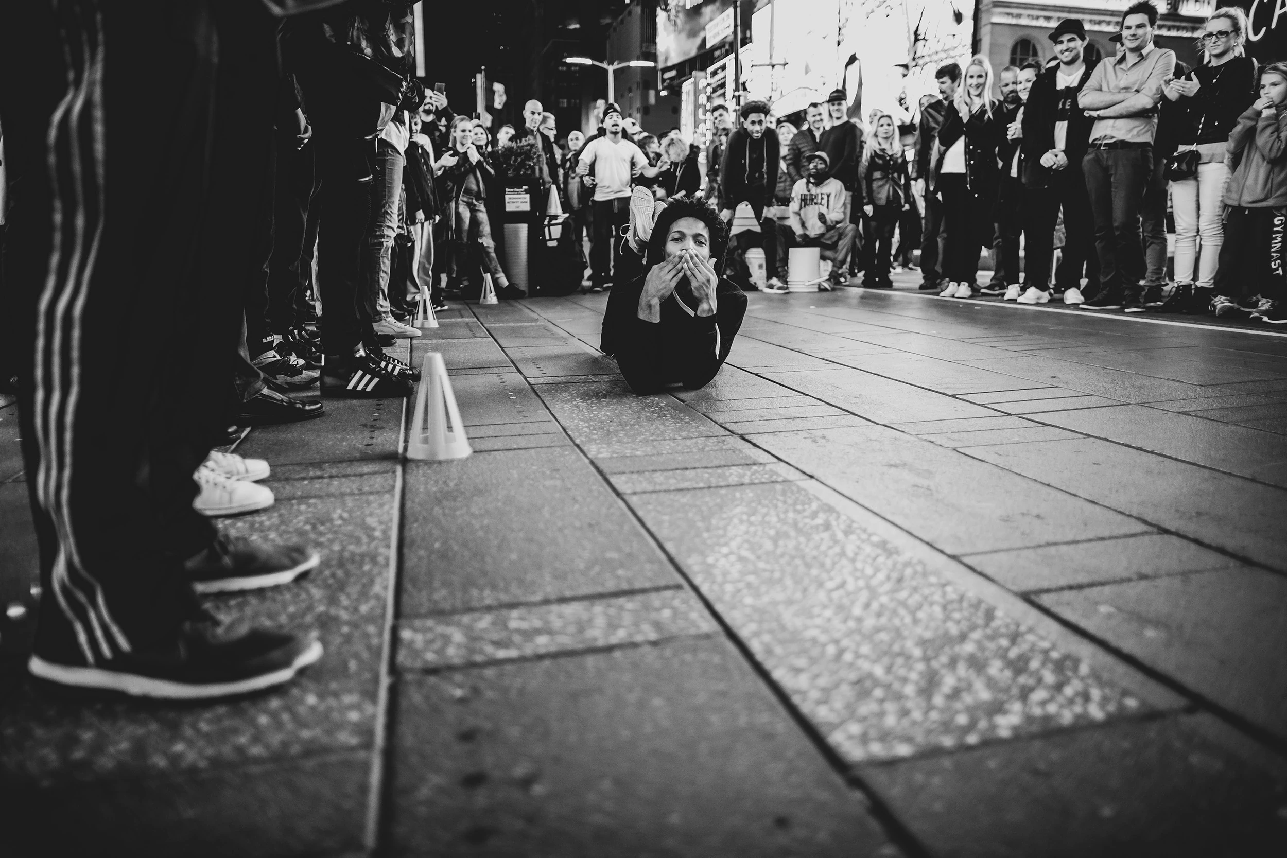In the foreground a passer-by's legs, in the distance the crowd along the pavement.