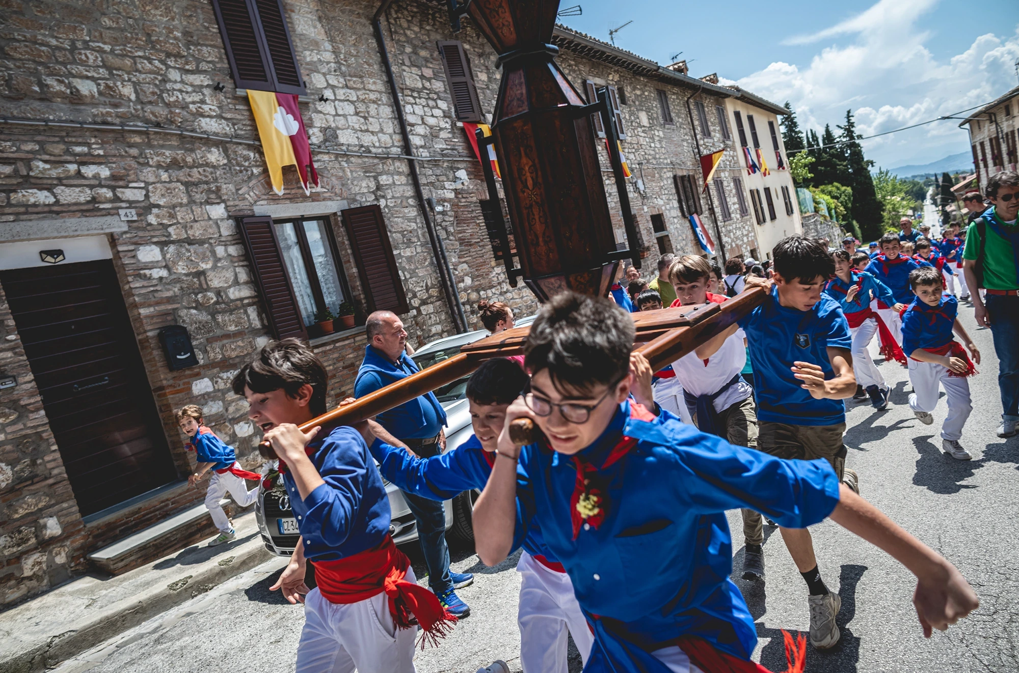 Young ceraioli in blue shirts carry a shaft on their shoulders down the street.
