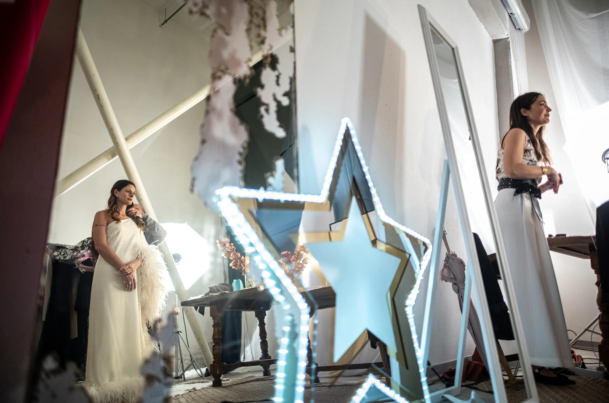 Among mirrors and a lit star, the bride and a friend in the room.