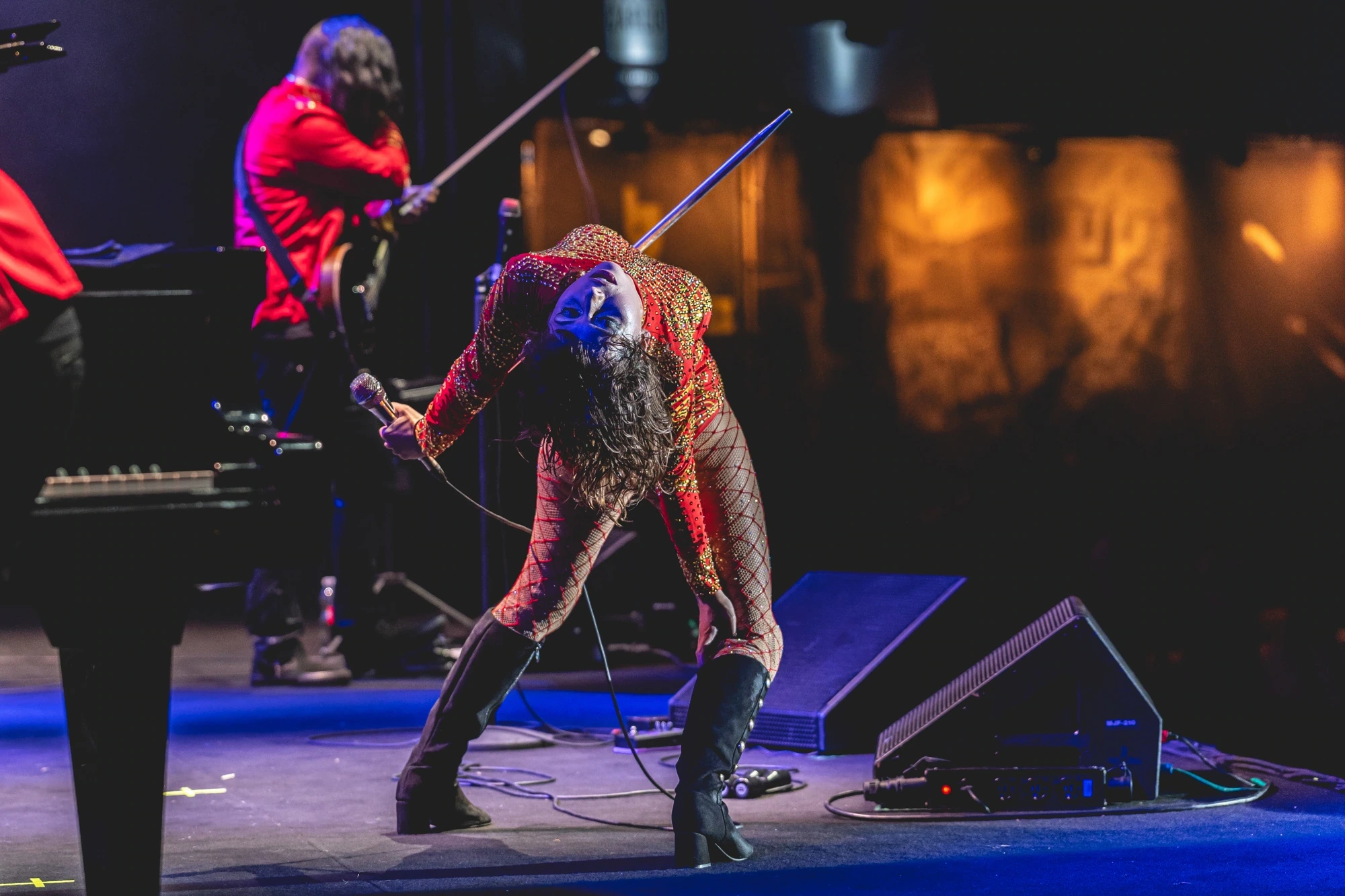Bent over the microphone in a patterned suit, on the theatre stage.