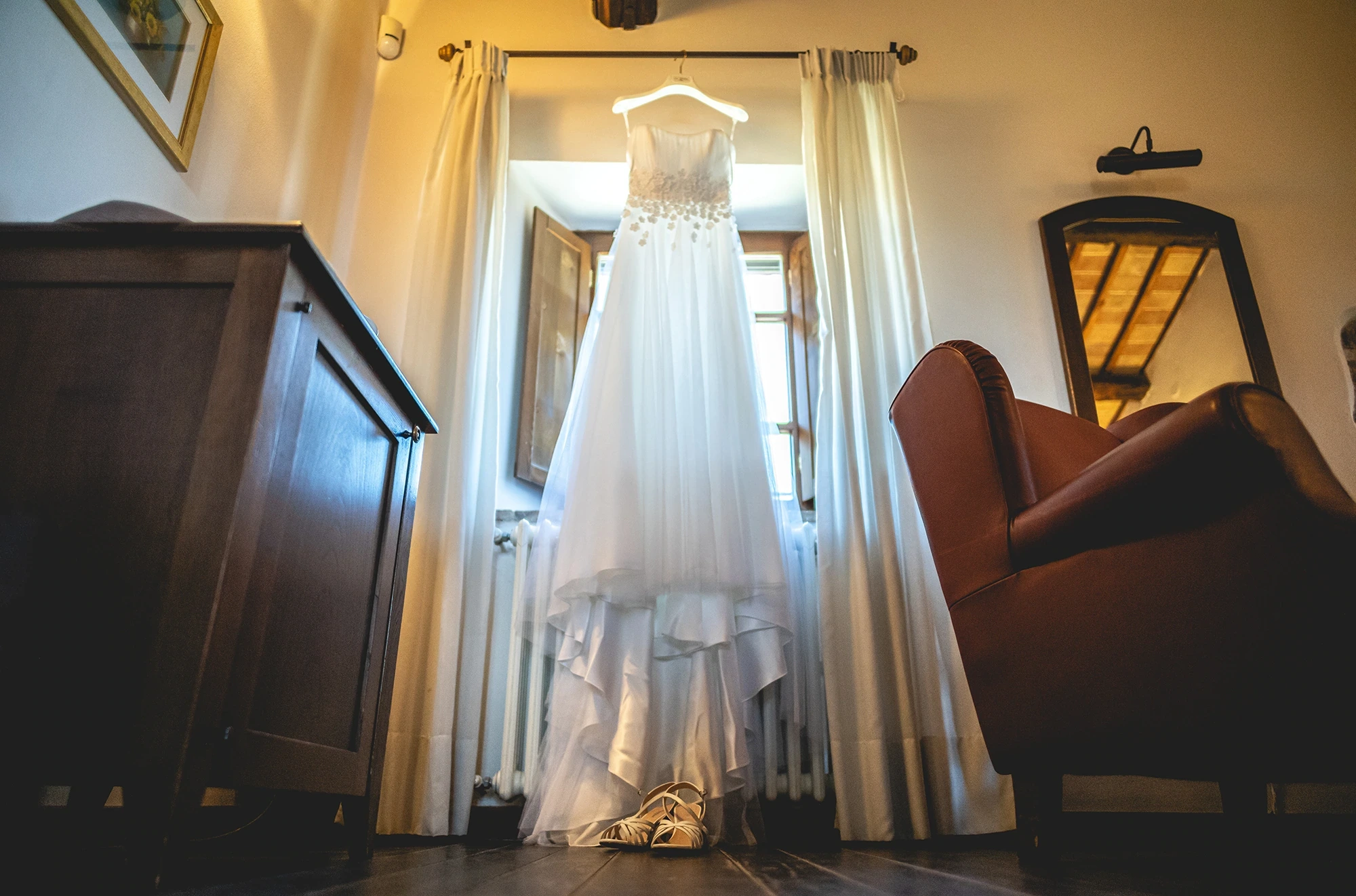 The dress hanging in the window, between the wardrobe and the armchair.