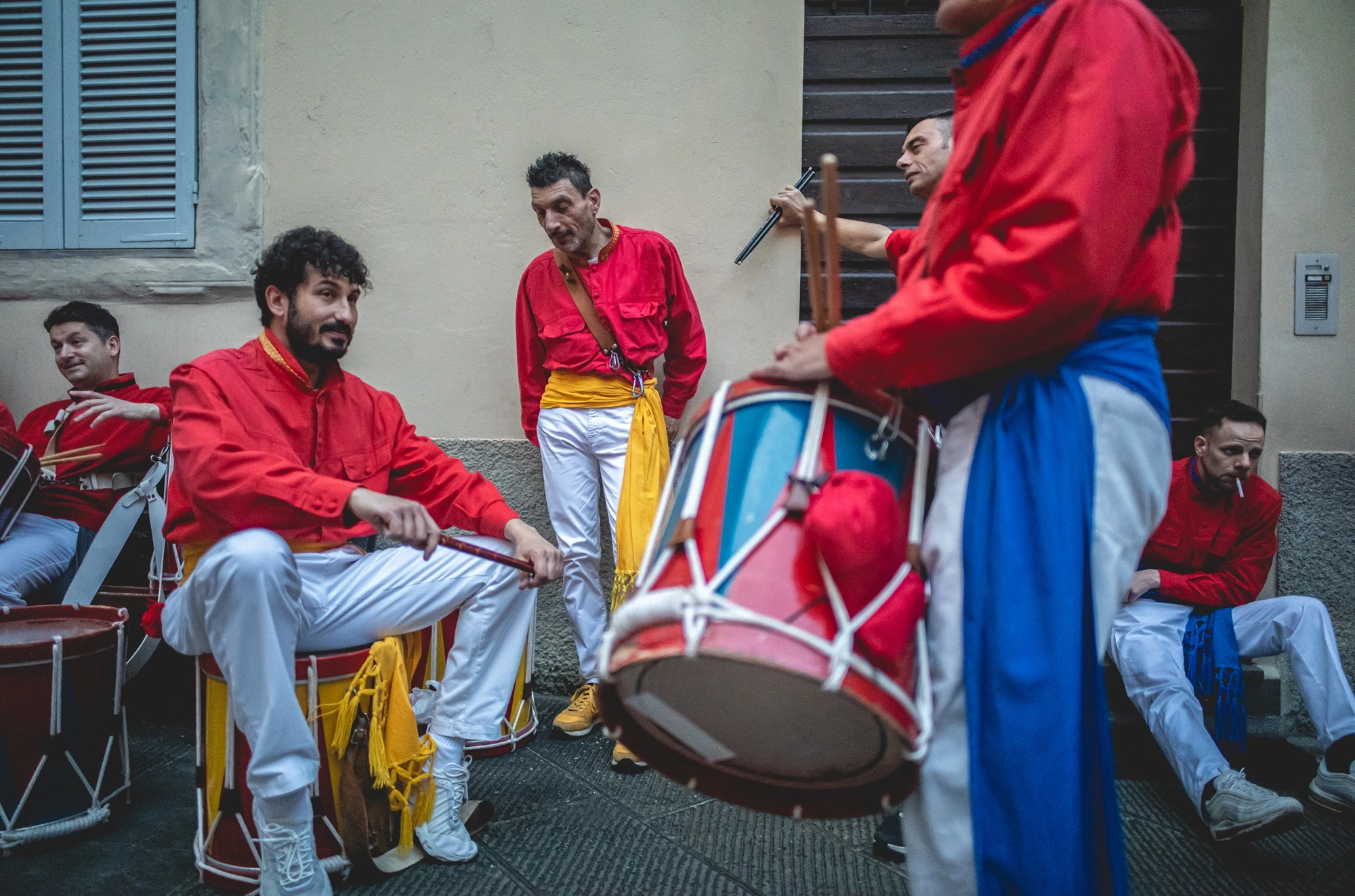 The drummers in red jackets, their drums resting on their legs.