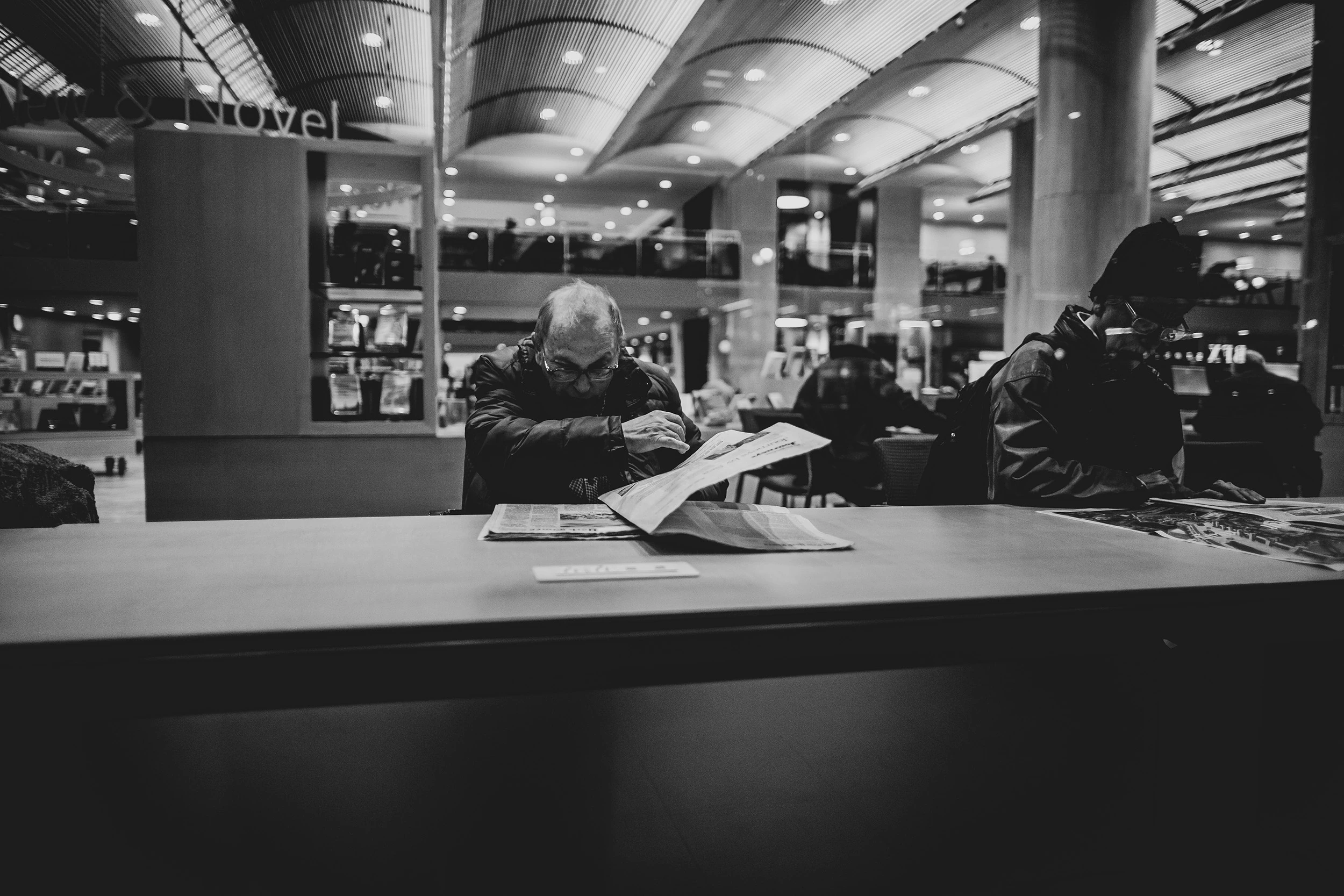 In a large public hall, people at the tables beyond an empty counter.