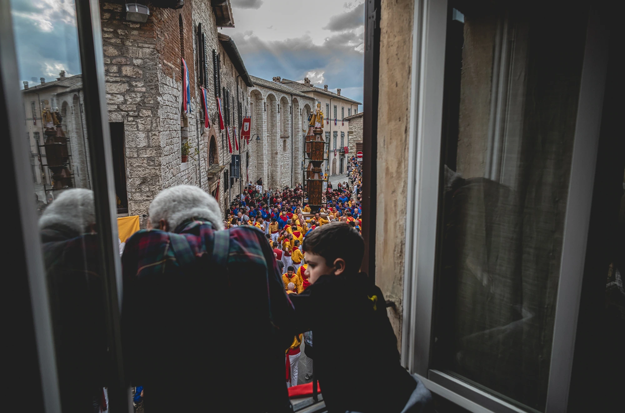 From inside a window, a family watches the feast pass in the street.