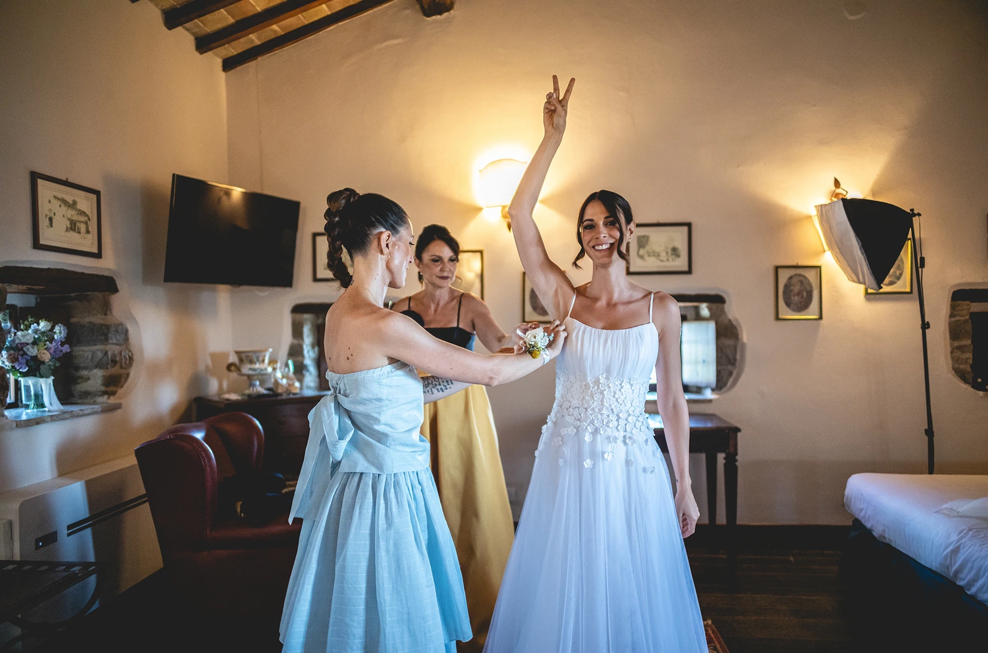 In the bedroom, the bride raises an arm among friends in pale blue.
