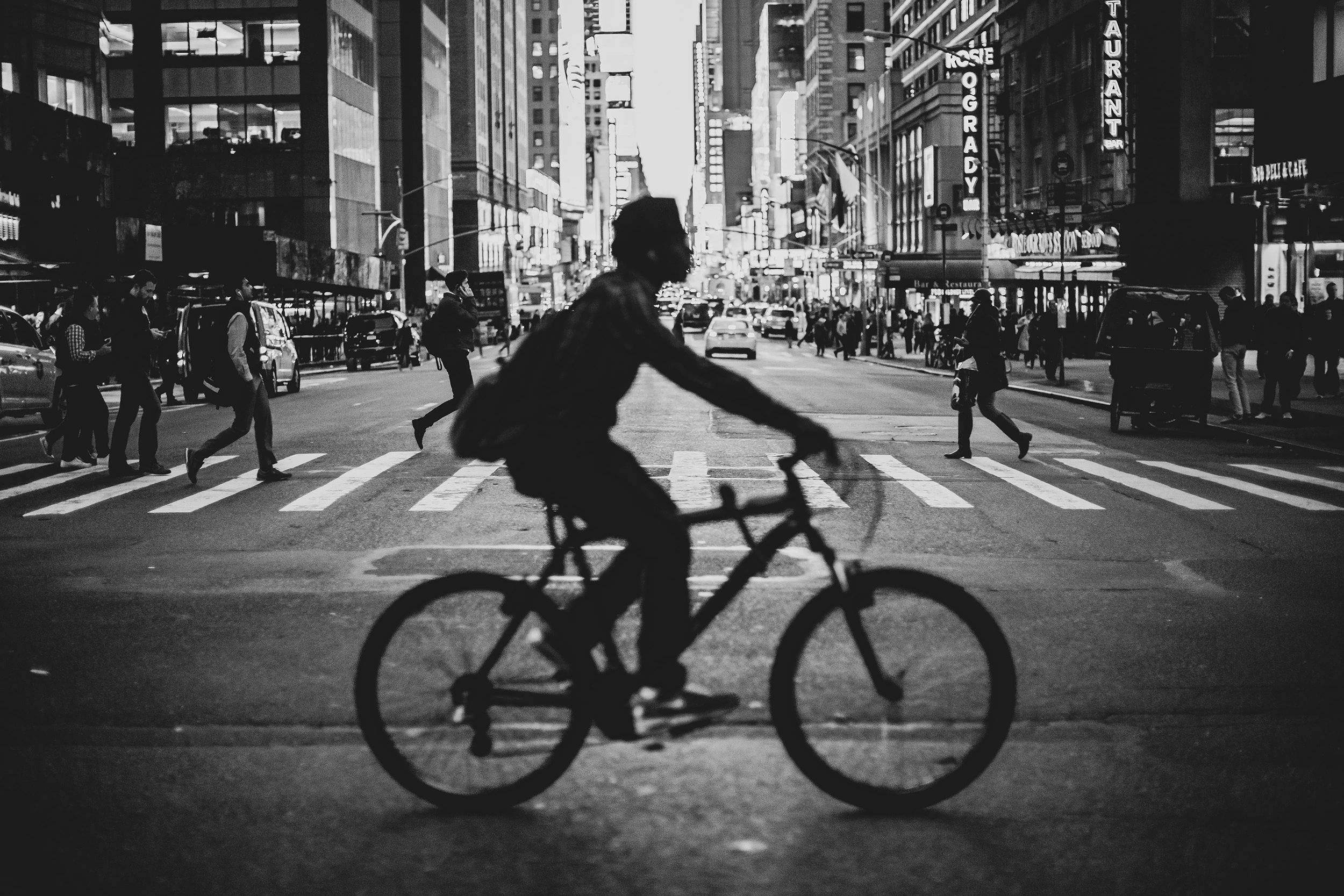 A cyclist crosses the intersection at night, among the lights of the billboards.