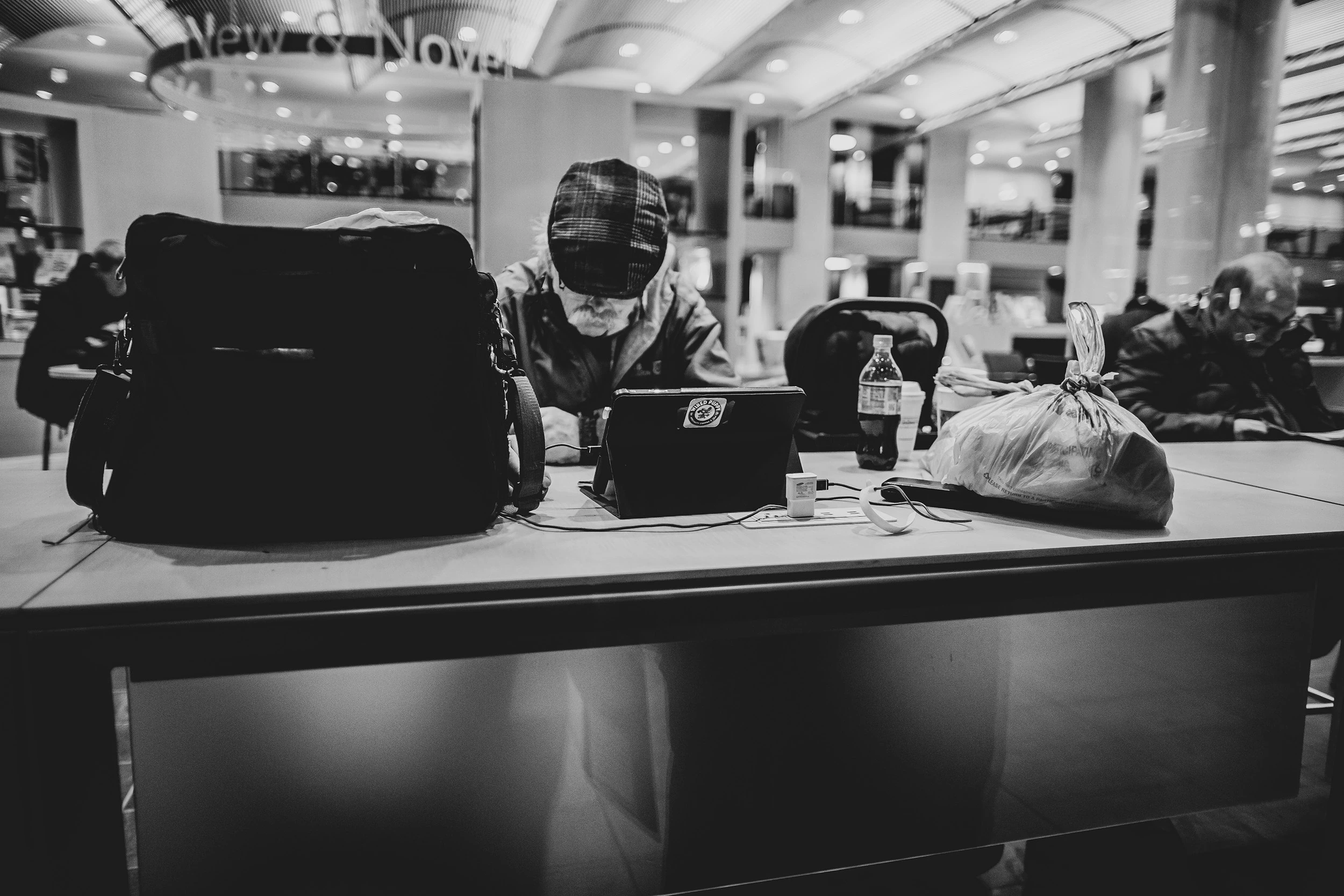 At a concourse counter, a hooded person among bags and a laptop.