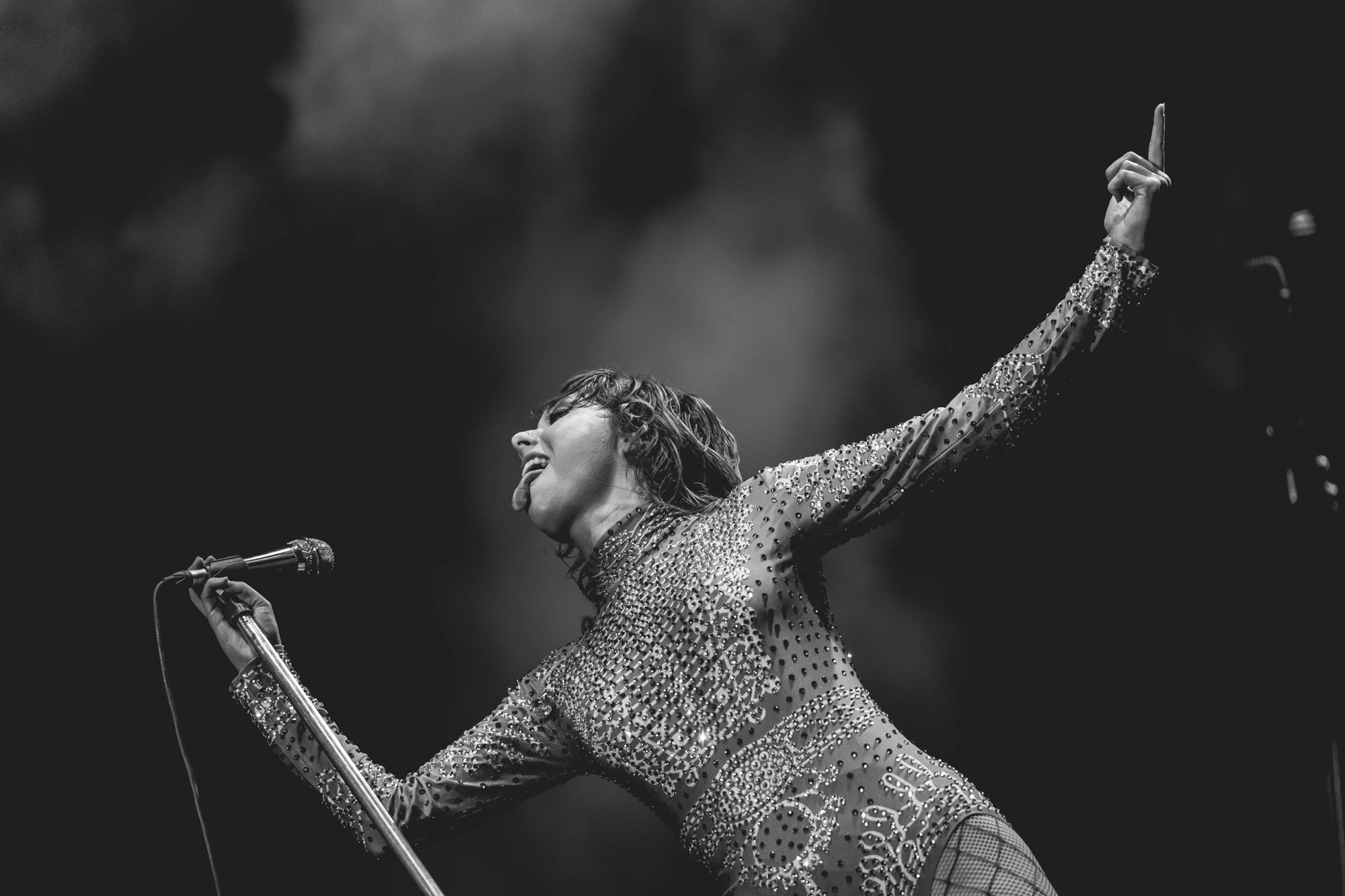 In a sequinned dress, one arm raised above the microphone.