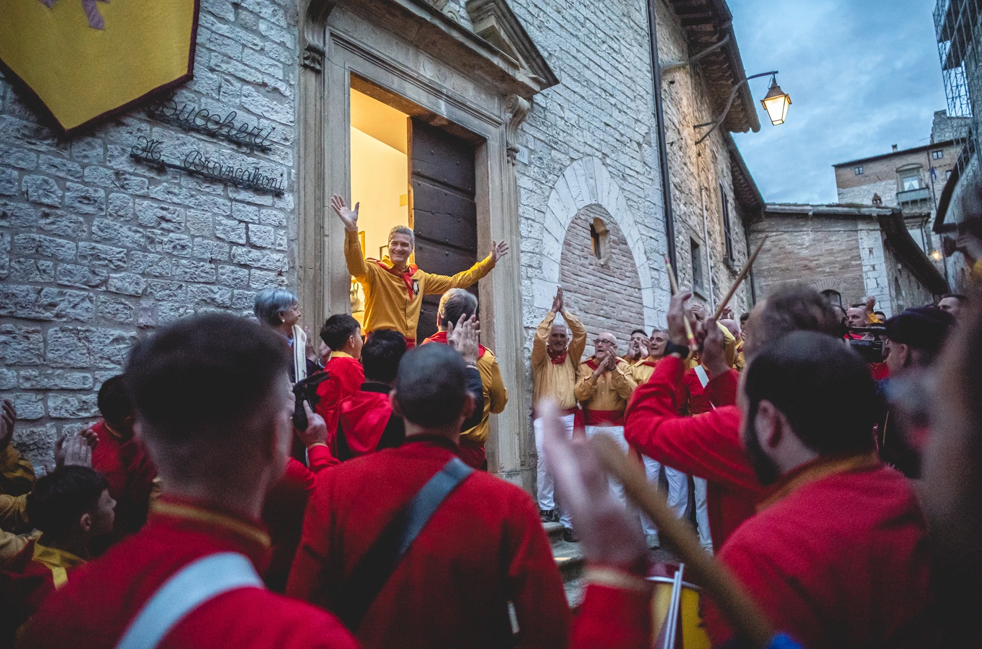 The ceraioli in red and yellow press before the doorway, arms raised.