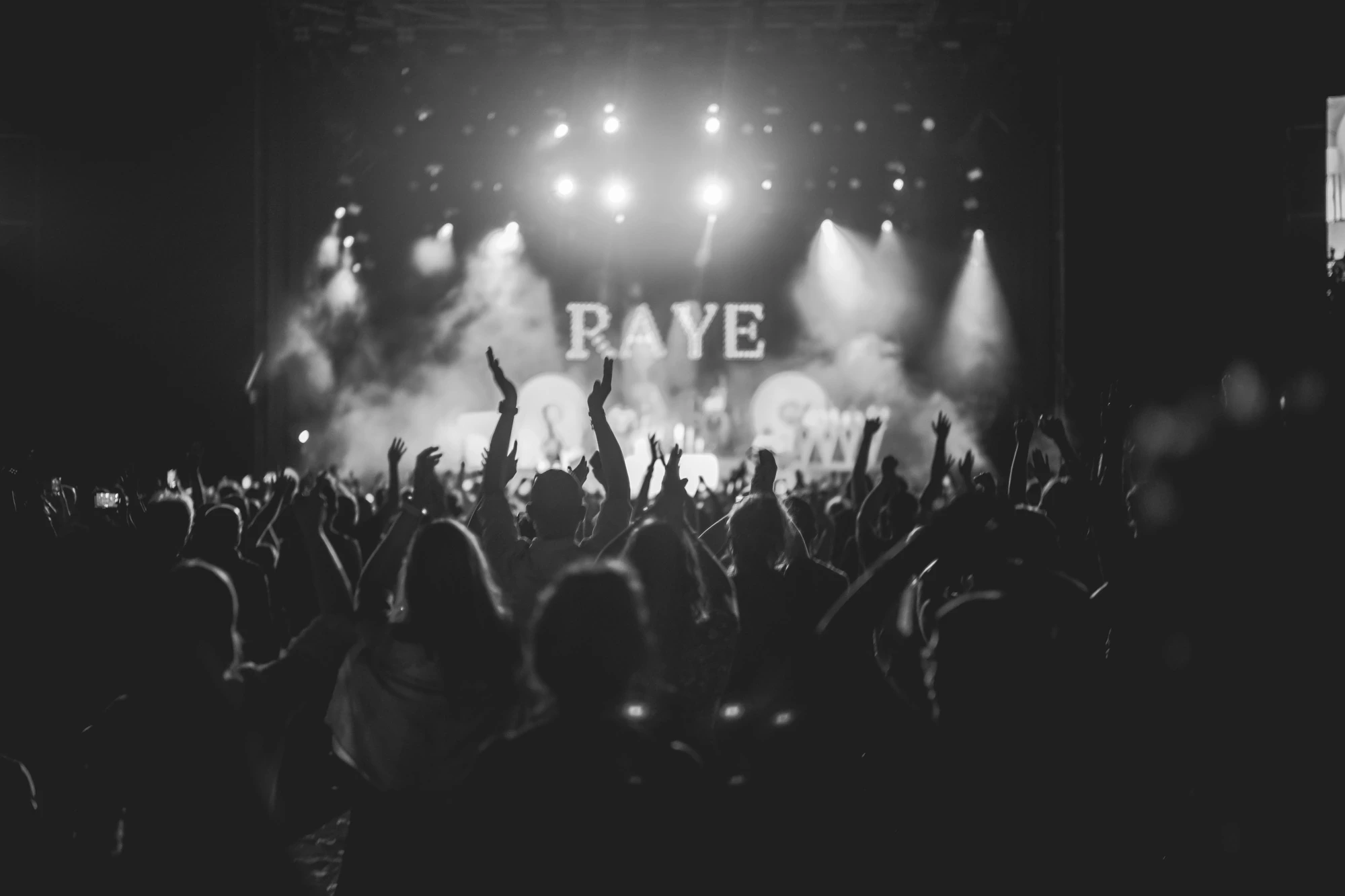 The audience with hands raised in front of the lit stage.