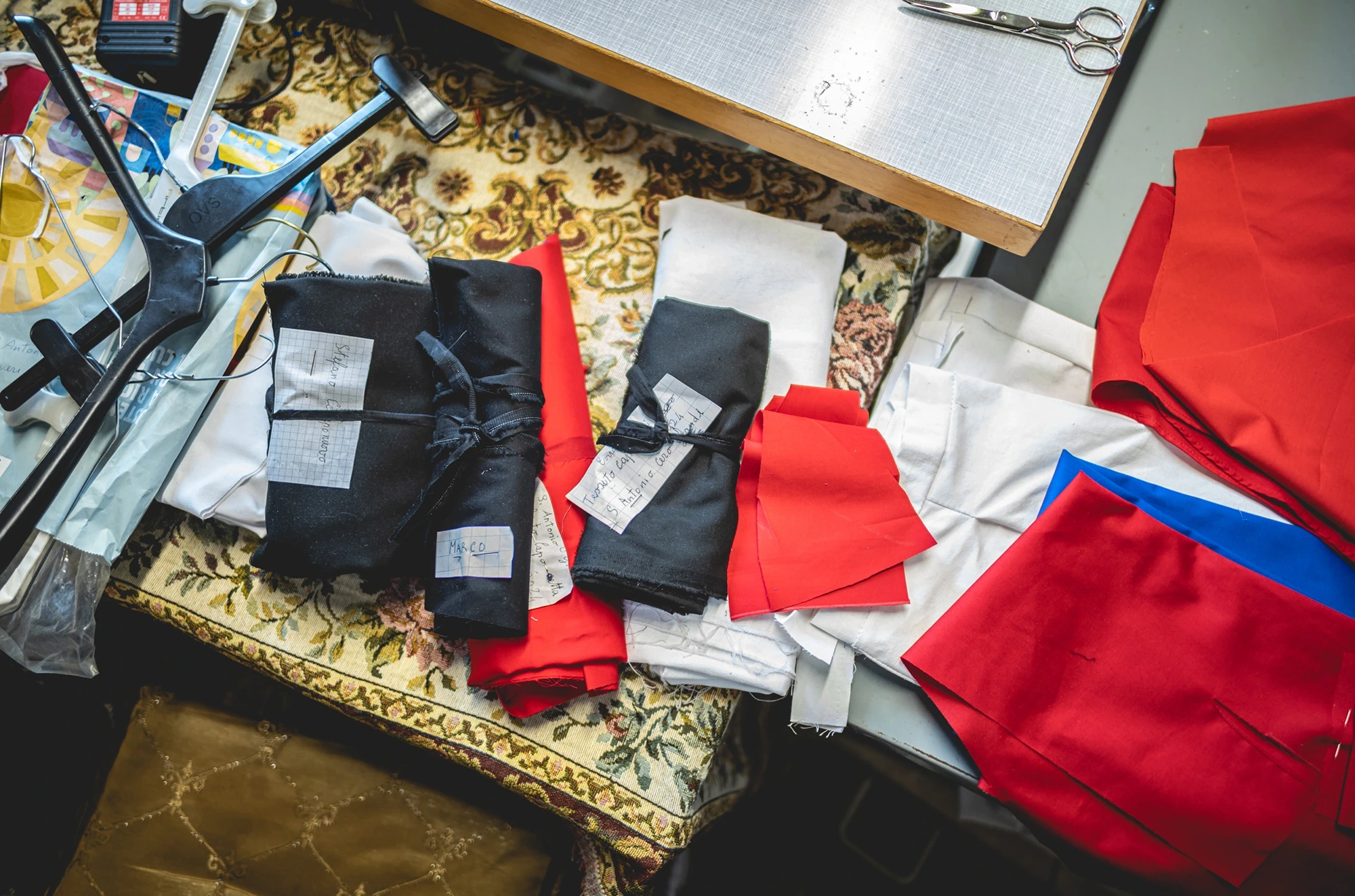 On a table, the folded sashes and the red and black cloth, with scissors.
