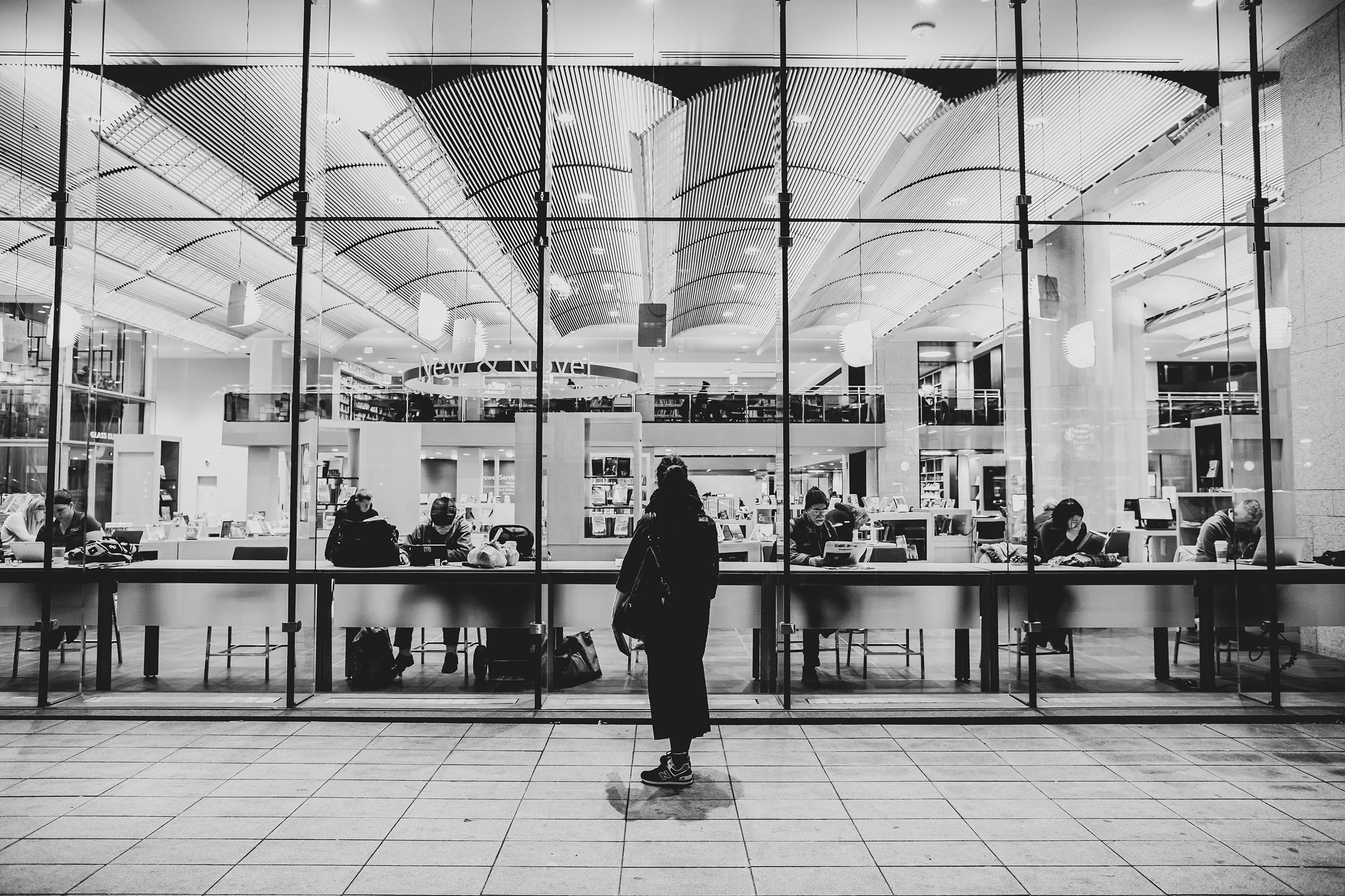 Outside a glass wall, a figure looks into the lit vaulted hall.