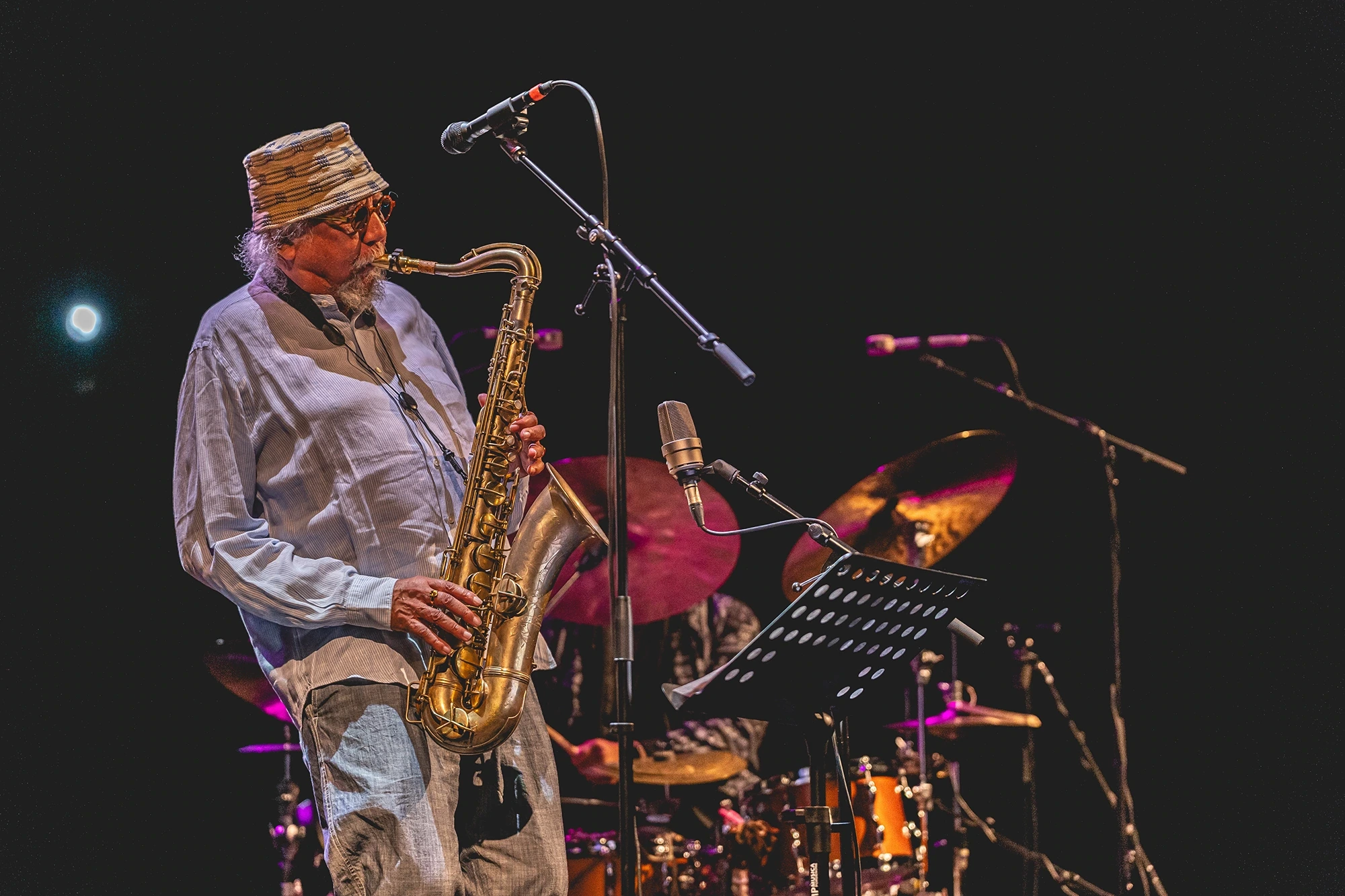 A saxophonist in a white shirt and embroidered cap.