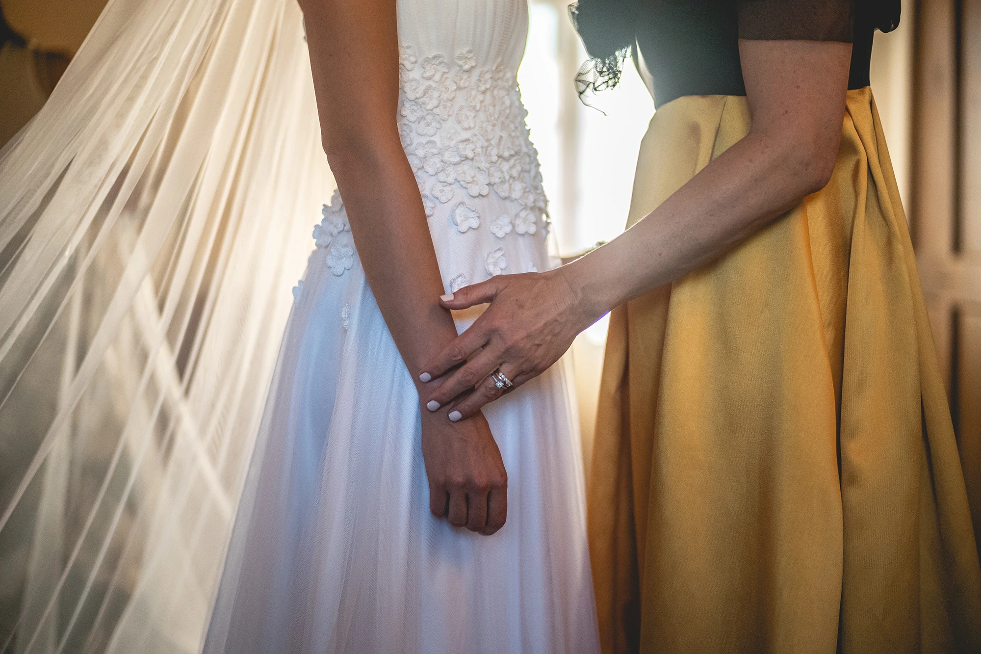 The bride's hands clasped over her dress, beside a yellow skirt.