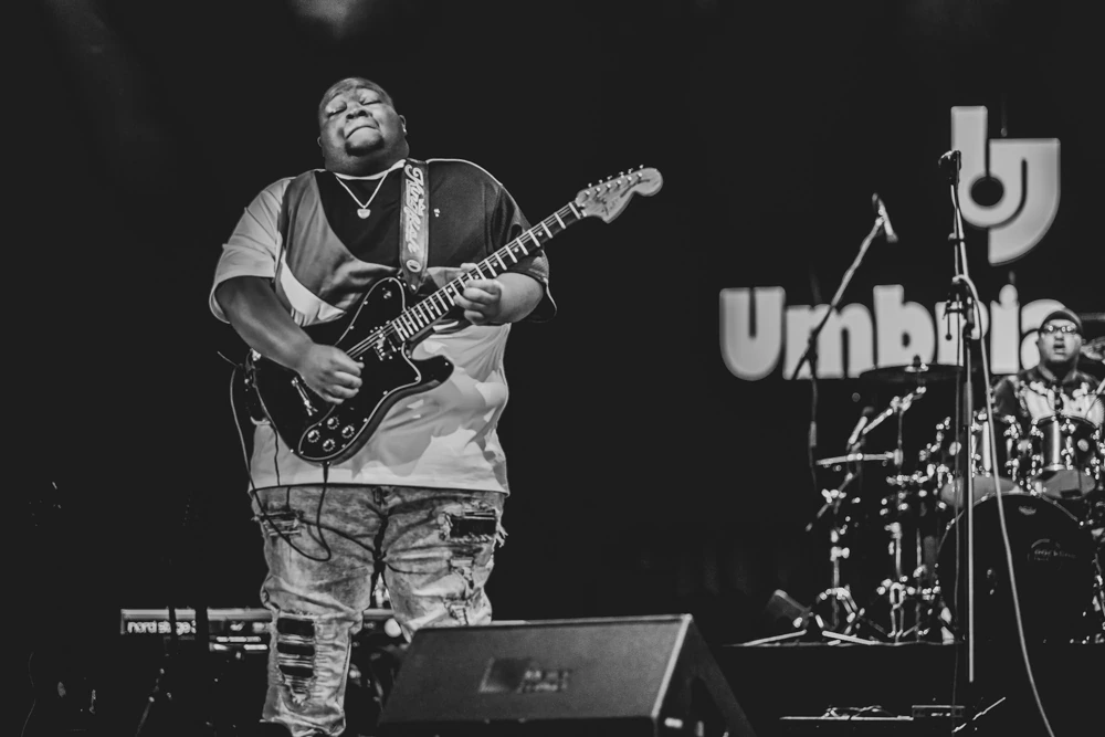 A guitarist on stage, the festival sign behind him.